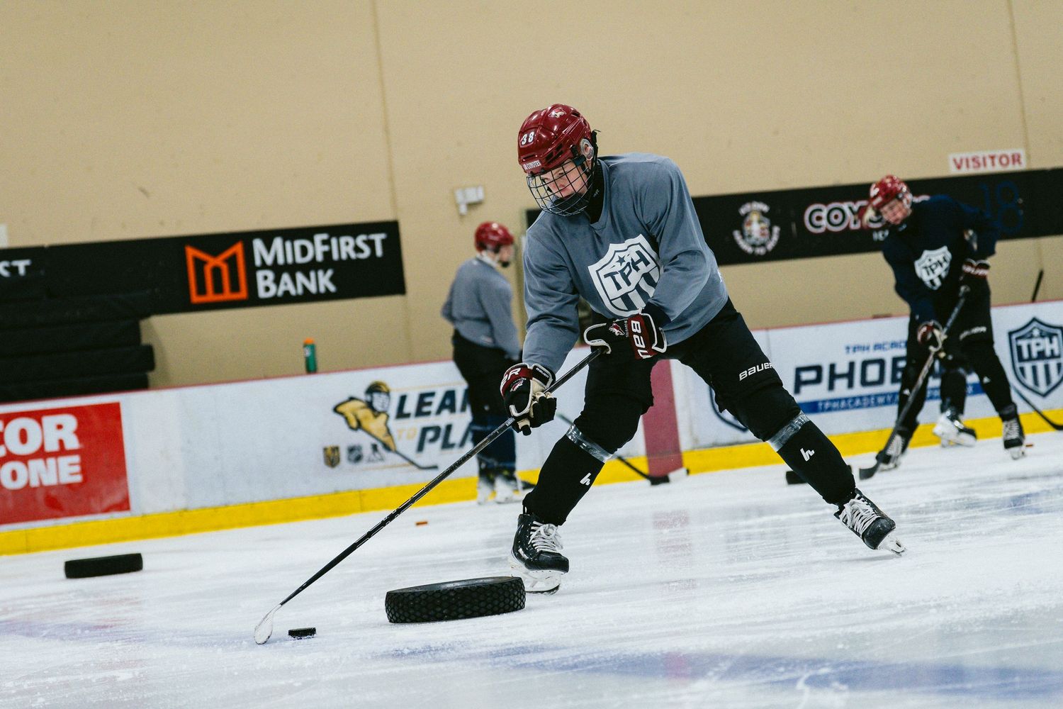 Young hockey player in gray jersey handles puck on ice during practice at MidFirst Bank arena.