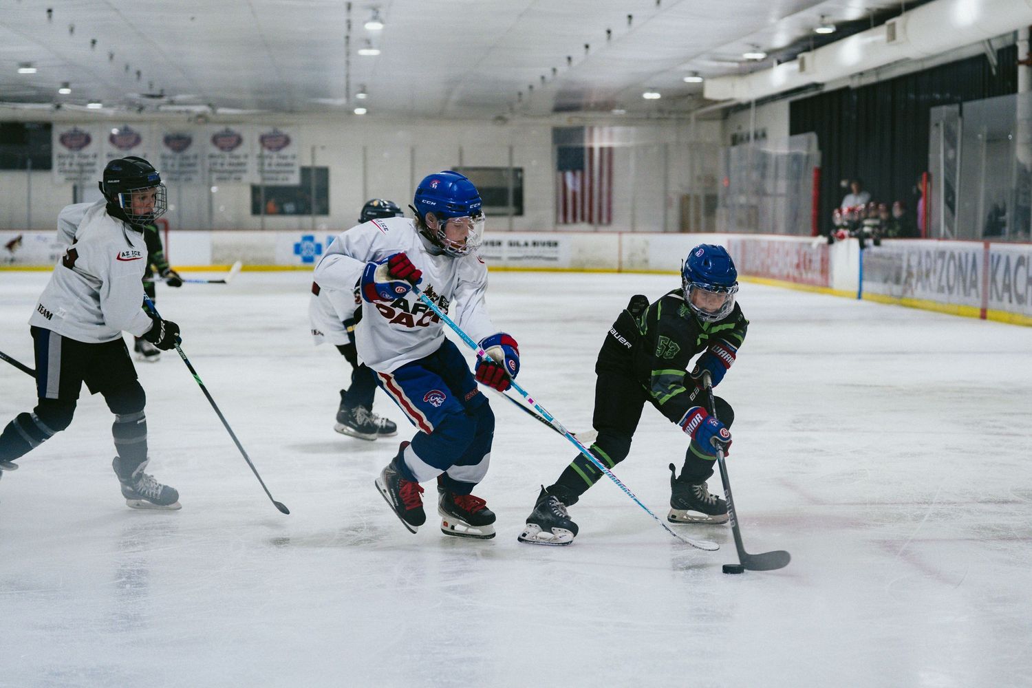 Youth ice hockey players compete for the puck during a game at an indoor ice skating rink.