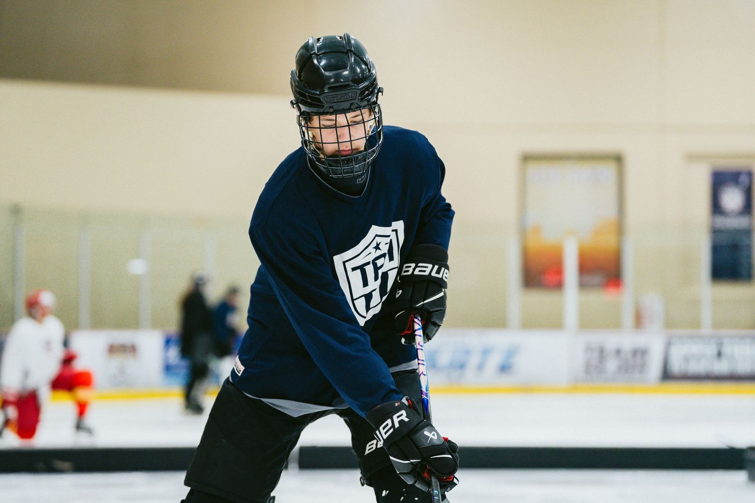 Young hockey player in navy Bauer gear skating during practice on indoor ice rink.