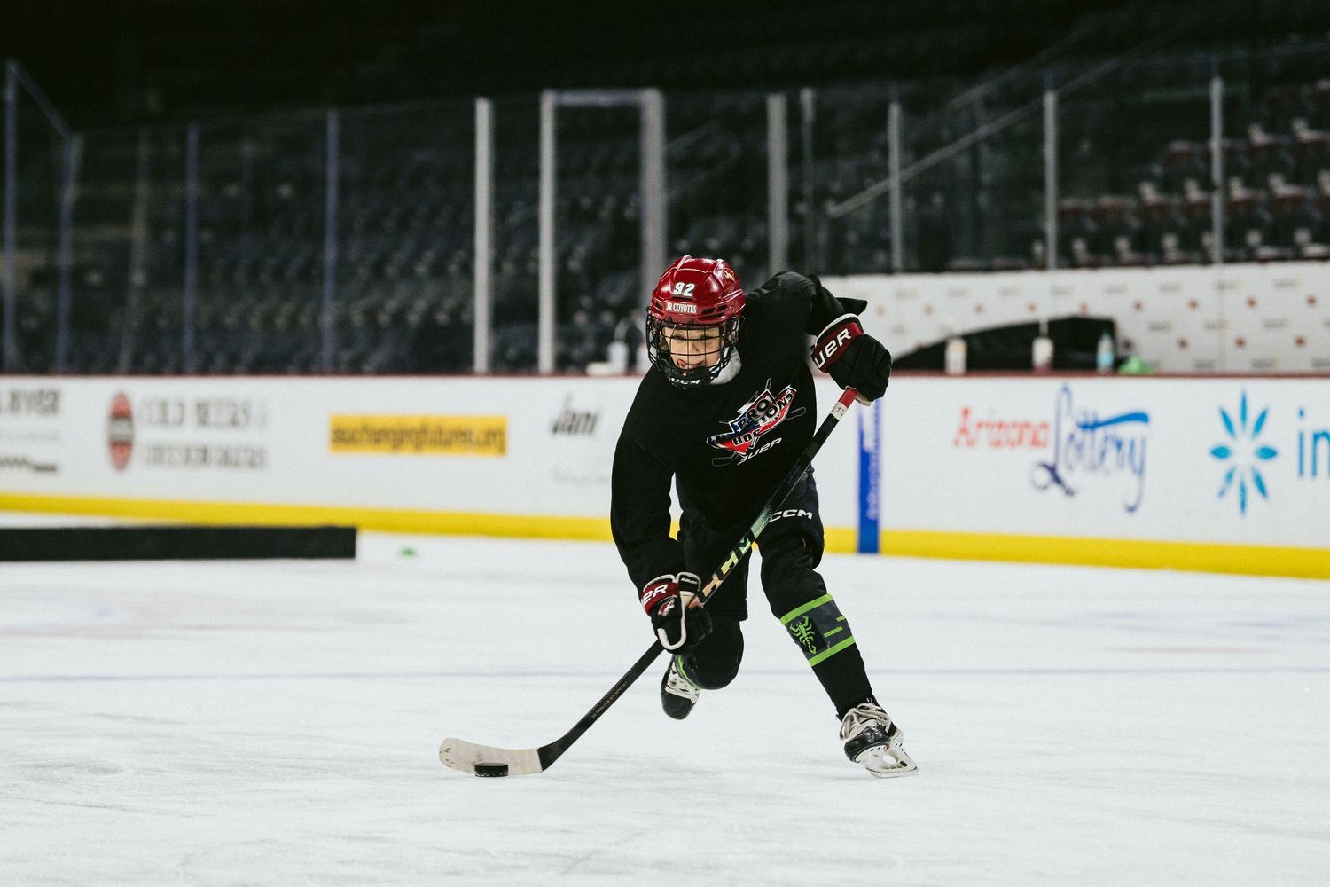 Young hockey player in black uniform skates with the puck during an indoor ice hockey practice.