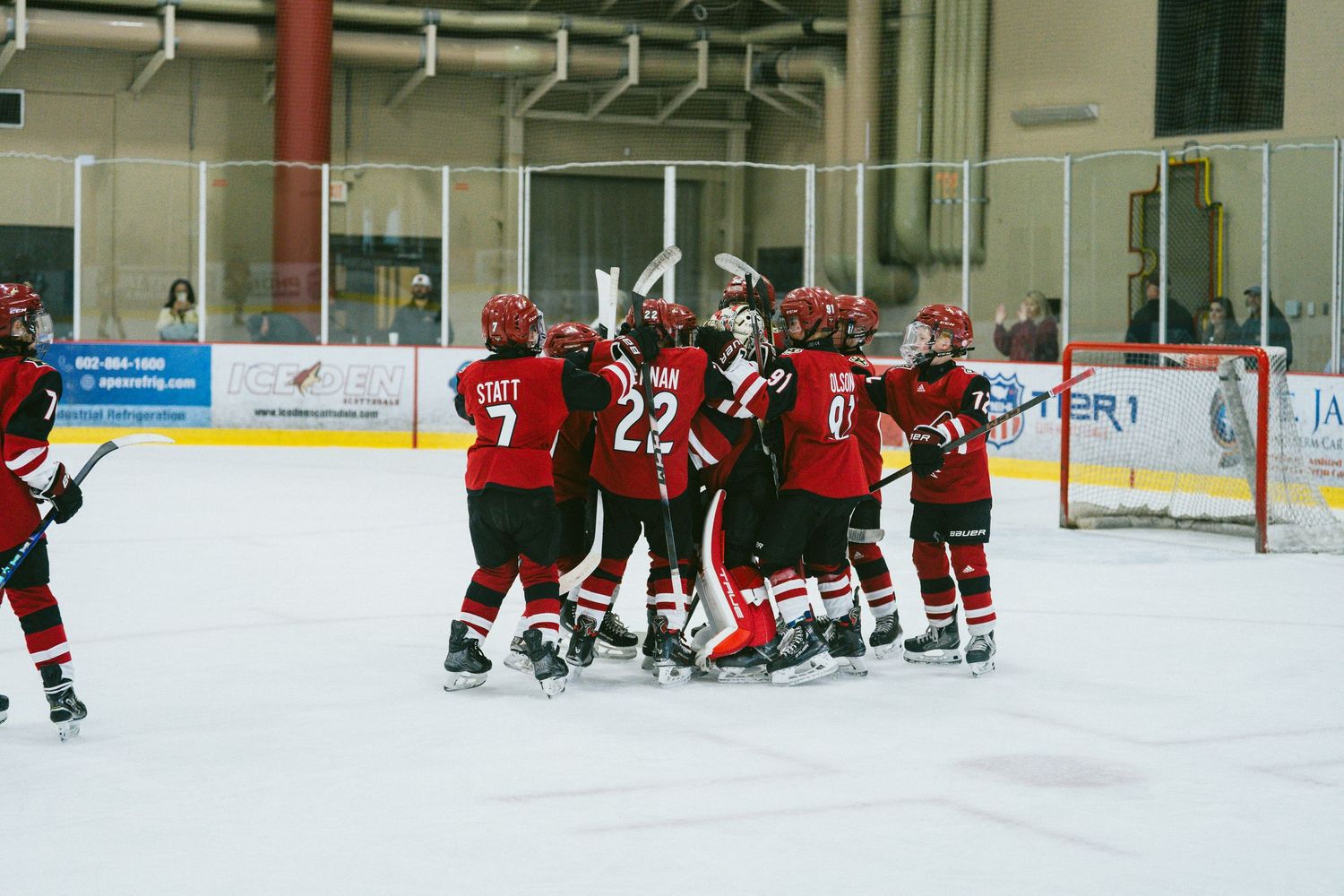 Hockey players in red and white uniforms line up along the boards during a game at an indoor ice rink.