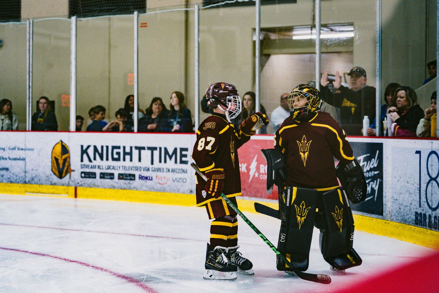 Wide view of an indoor ice hockey rink with spectators watching from behind glass barriers.