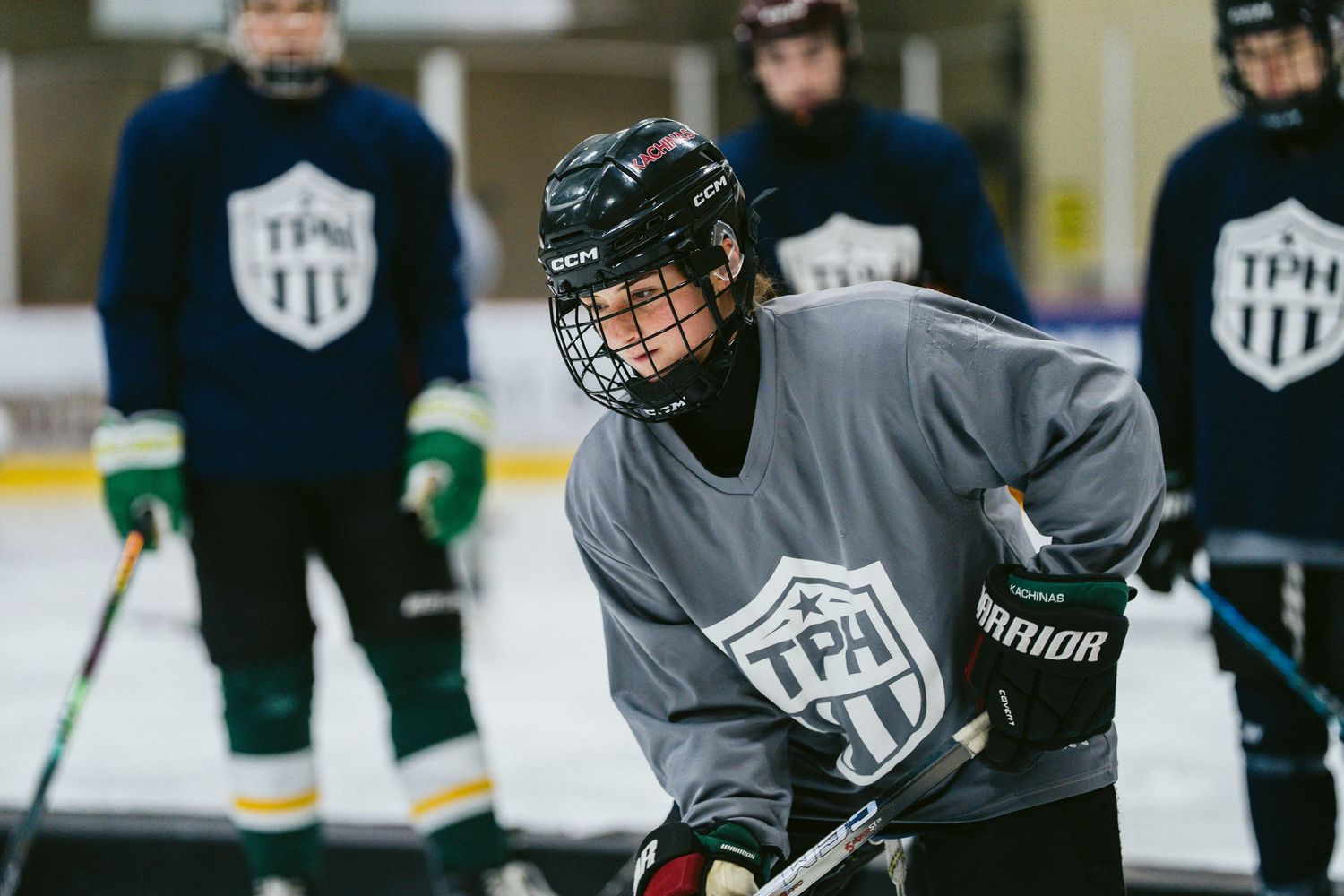 Young hockey player in TPH gray jersey and green helmet focuses during ice hockey practice drill.