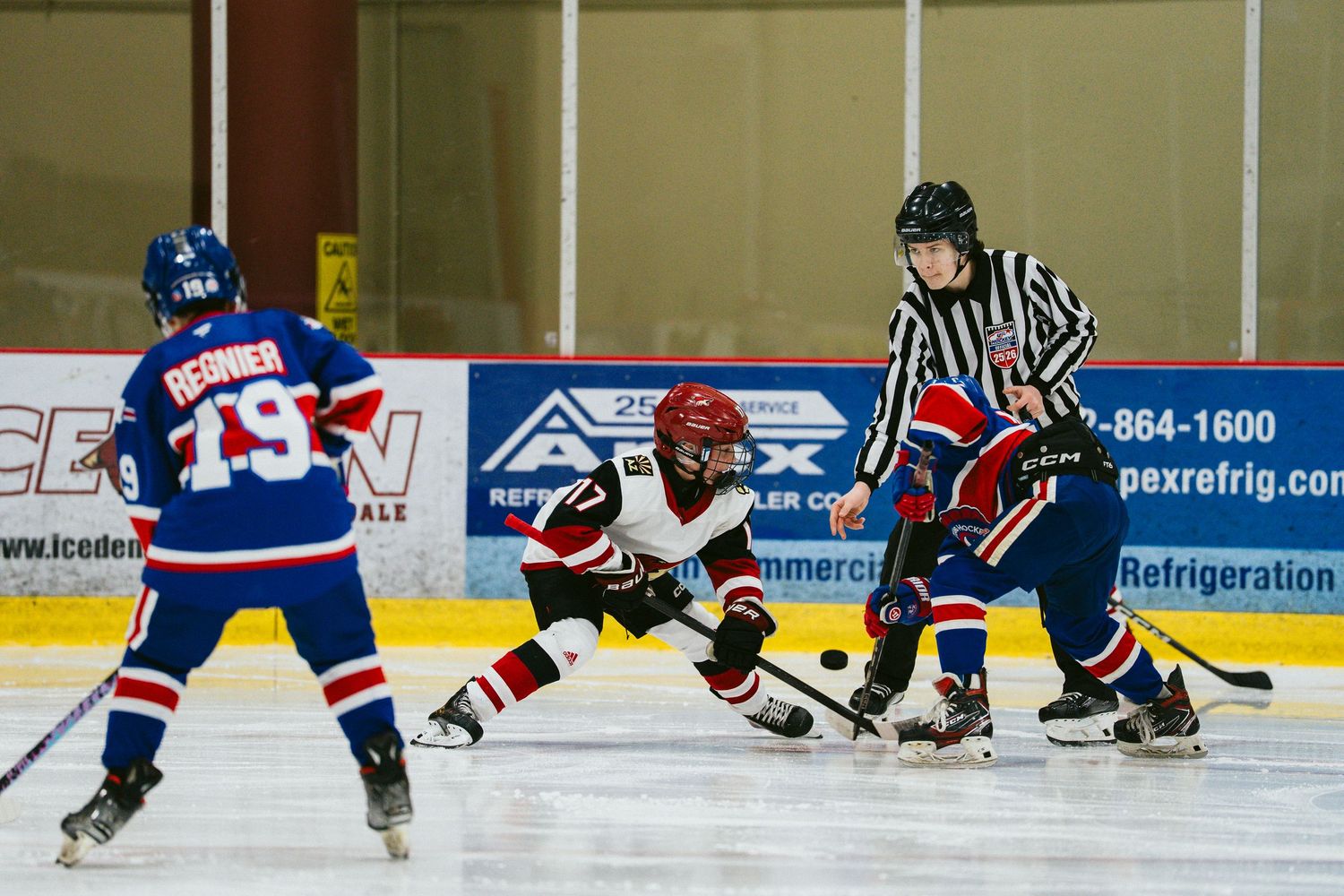 Youth hockey players in red and blue jerseys compete during an intense ice hockey match.