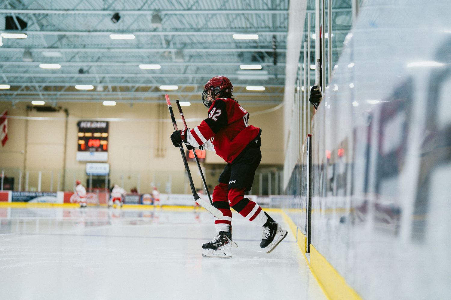 Hockey players in red and black uniforms practice on a brightly lit indoor ice rink.