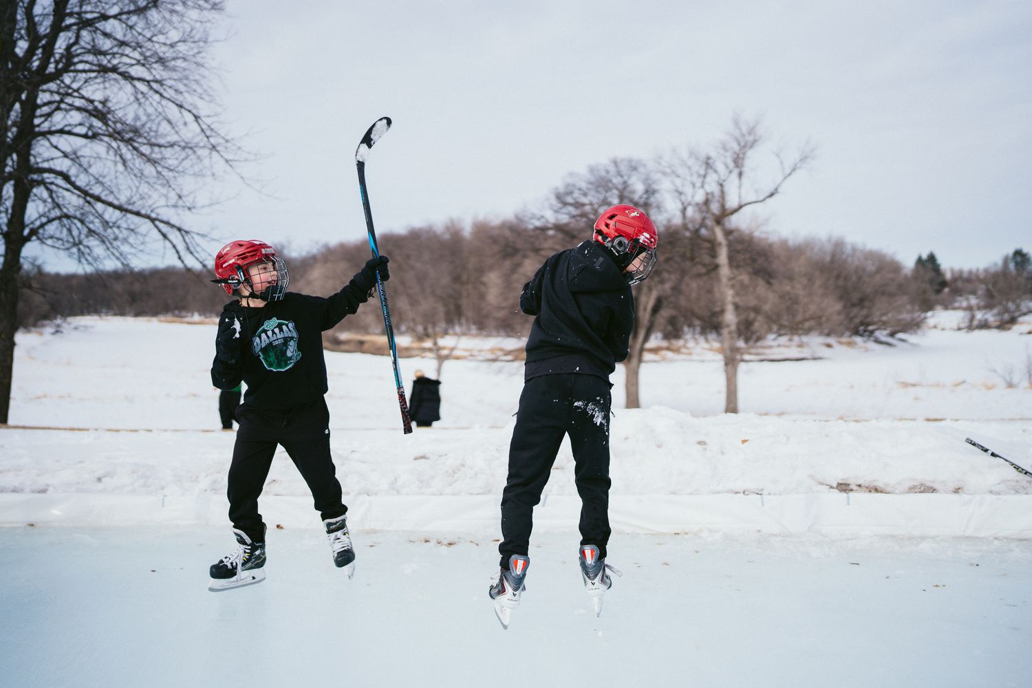 Two hockey players celebrating with raised sticks on a snowy outdoor rink.