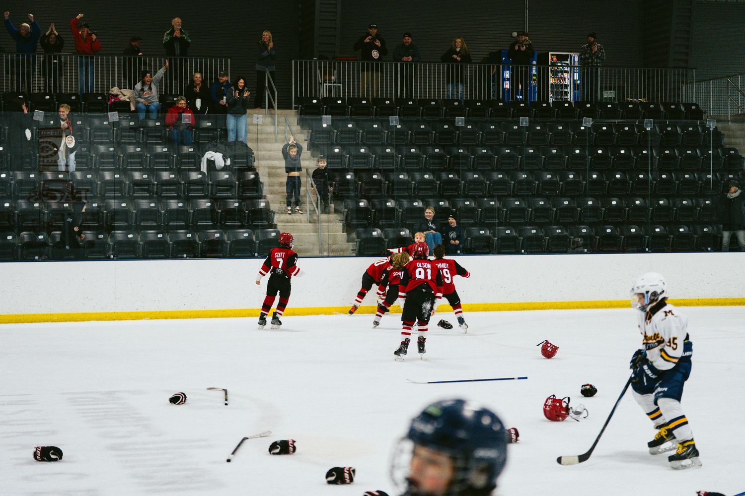 Youth hockey players in red jerseys spread across the ice during an indoor game.