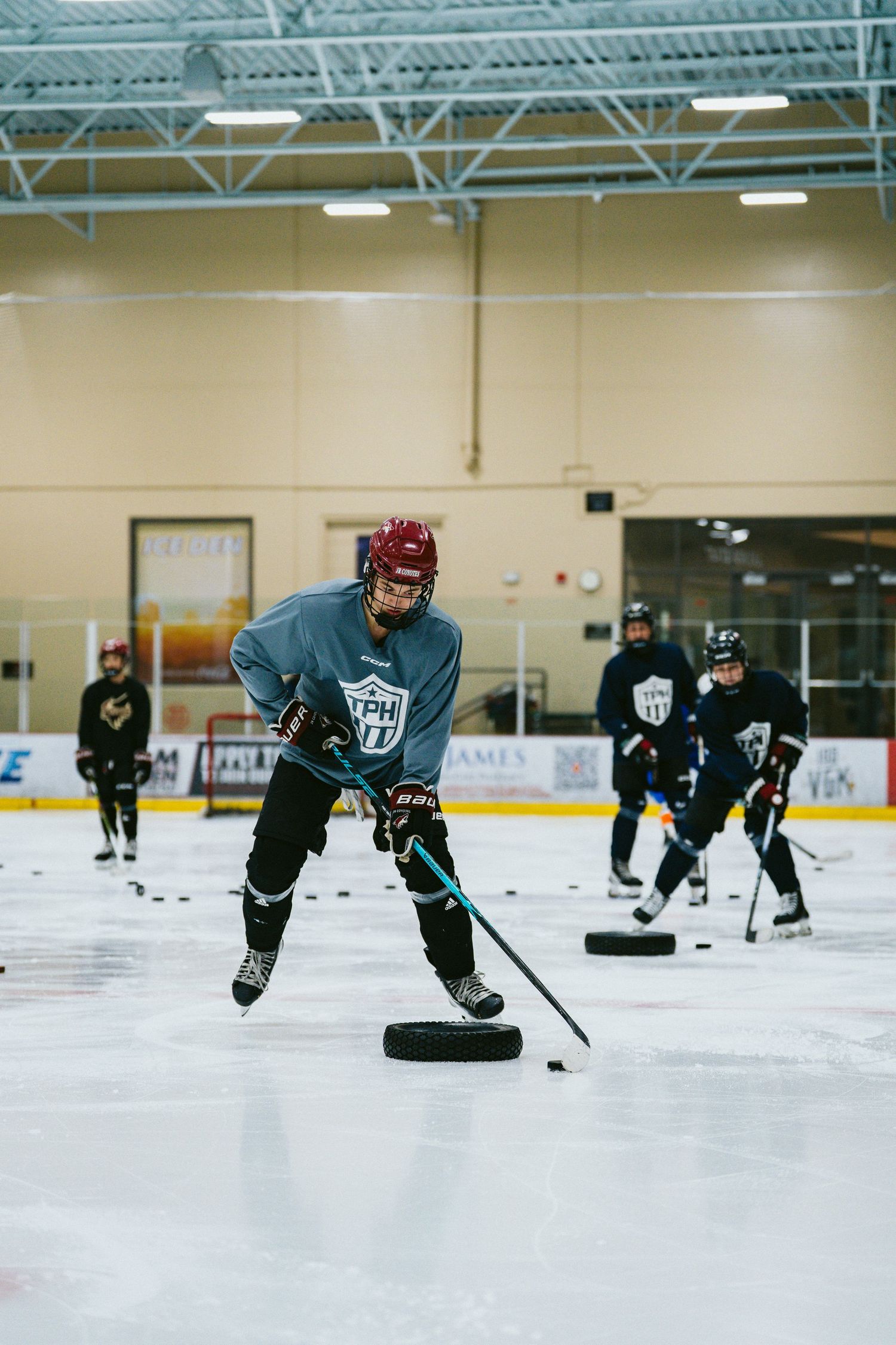 Hockey players practice skating and puck handling drills on an indoor ice rink during a team training session.