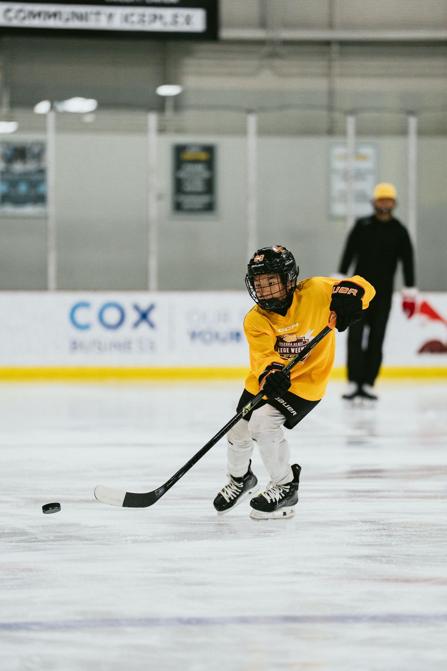 Young hockey player in yellow jersey controls the puck while skating on an indoor ice rink during practice.