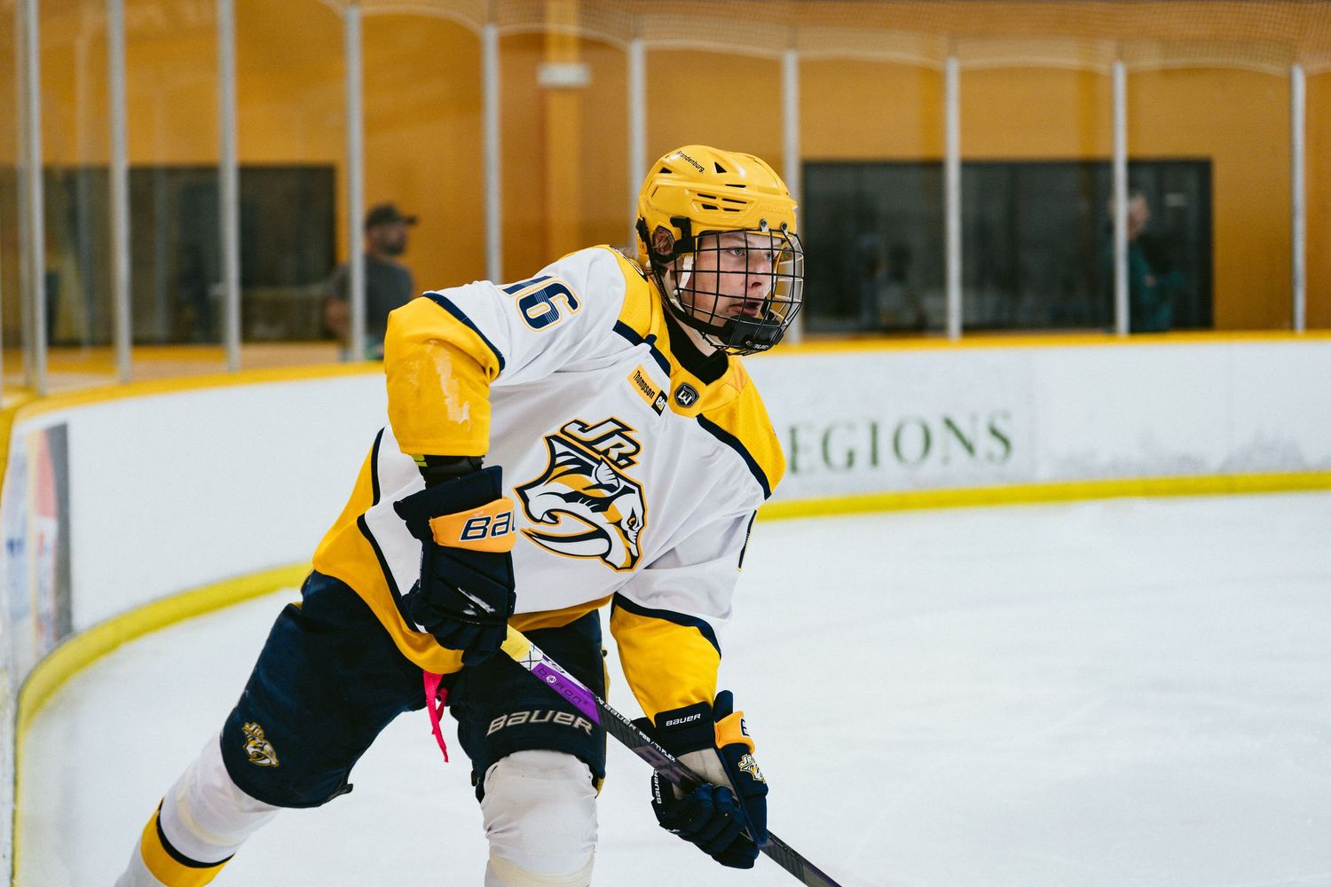 A hockey player in a gold and black uniform skates with a stick during an indoor ice hockey game.