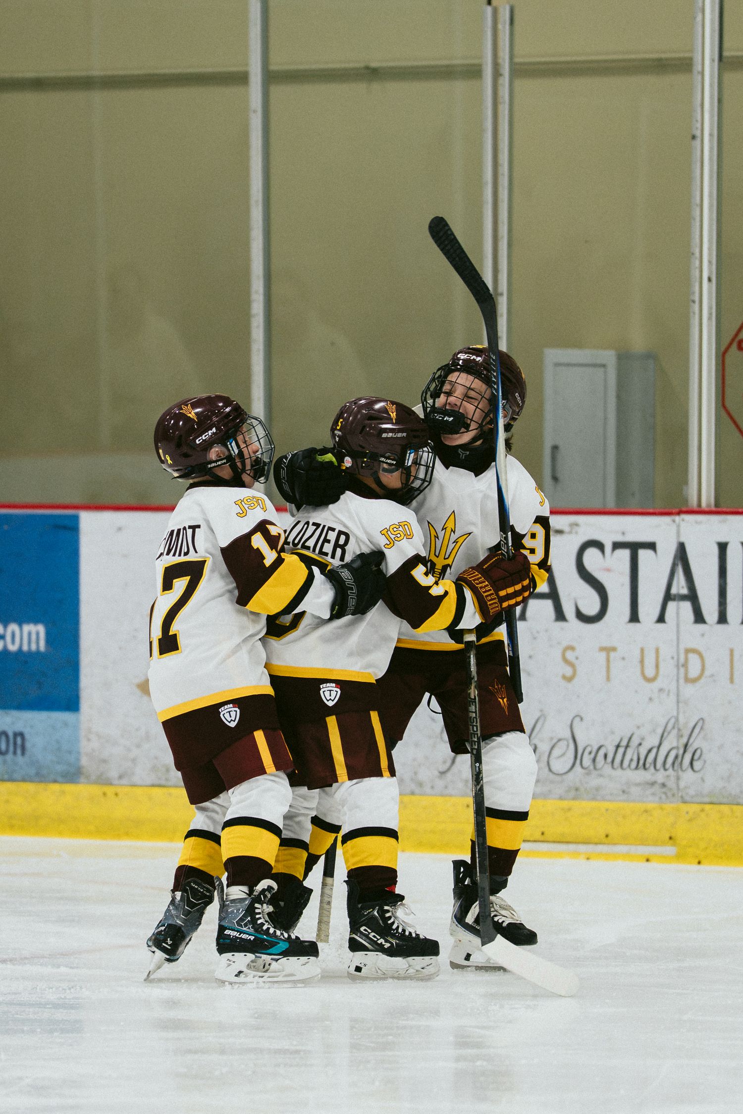 Arizona State Sun Devils hockey players celebrate a goal on the ice at Scottsdale rink in maroon and gold uniforms.
