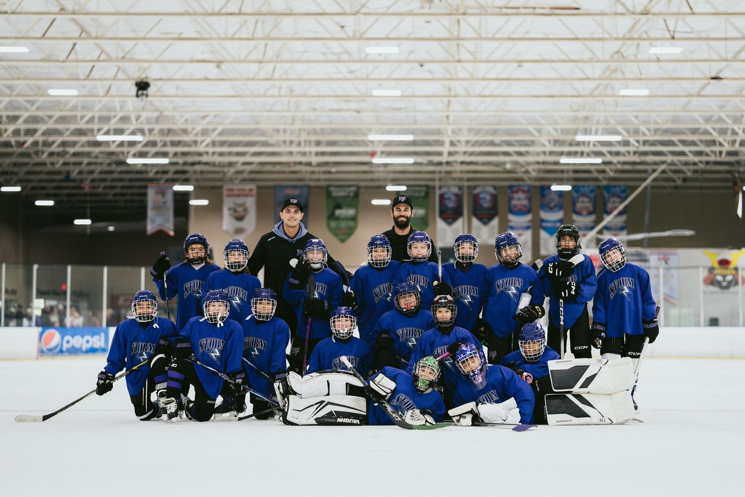 Youth hockey team in blue uniforms poses together on indoor ice rink for group photo.