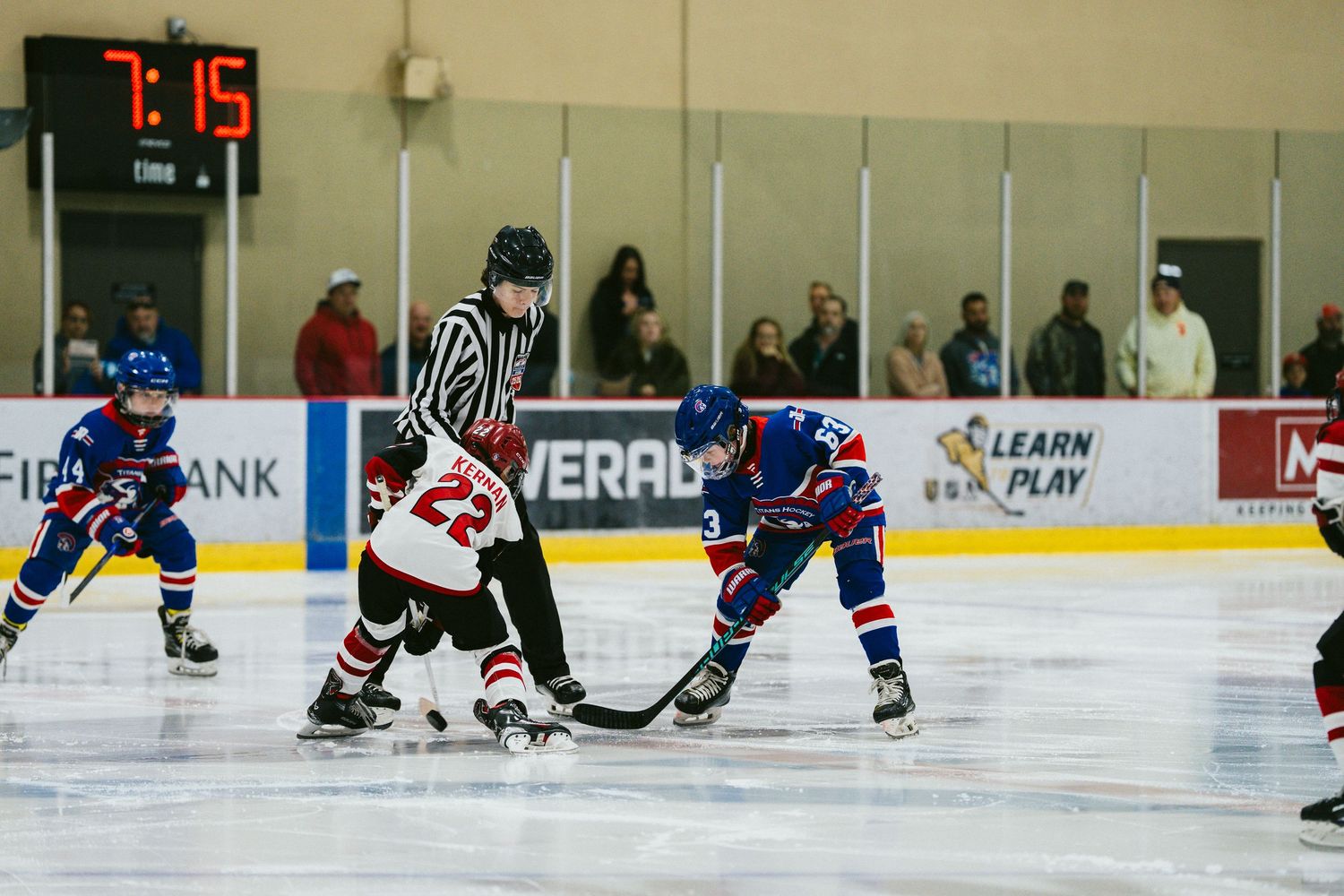 A referee oversees a face-off between two hockey players during a competitive match.