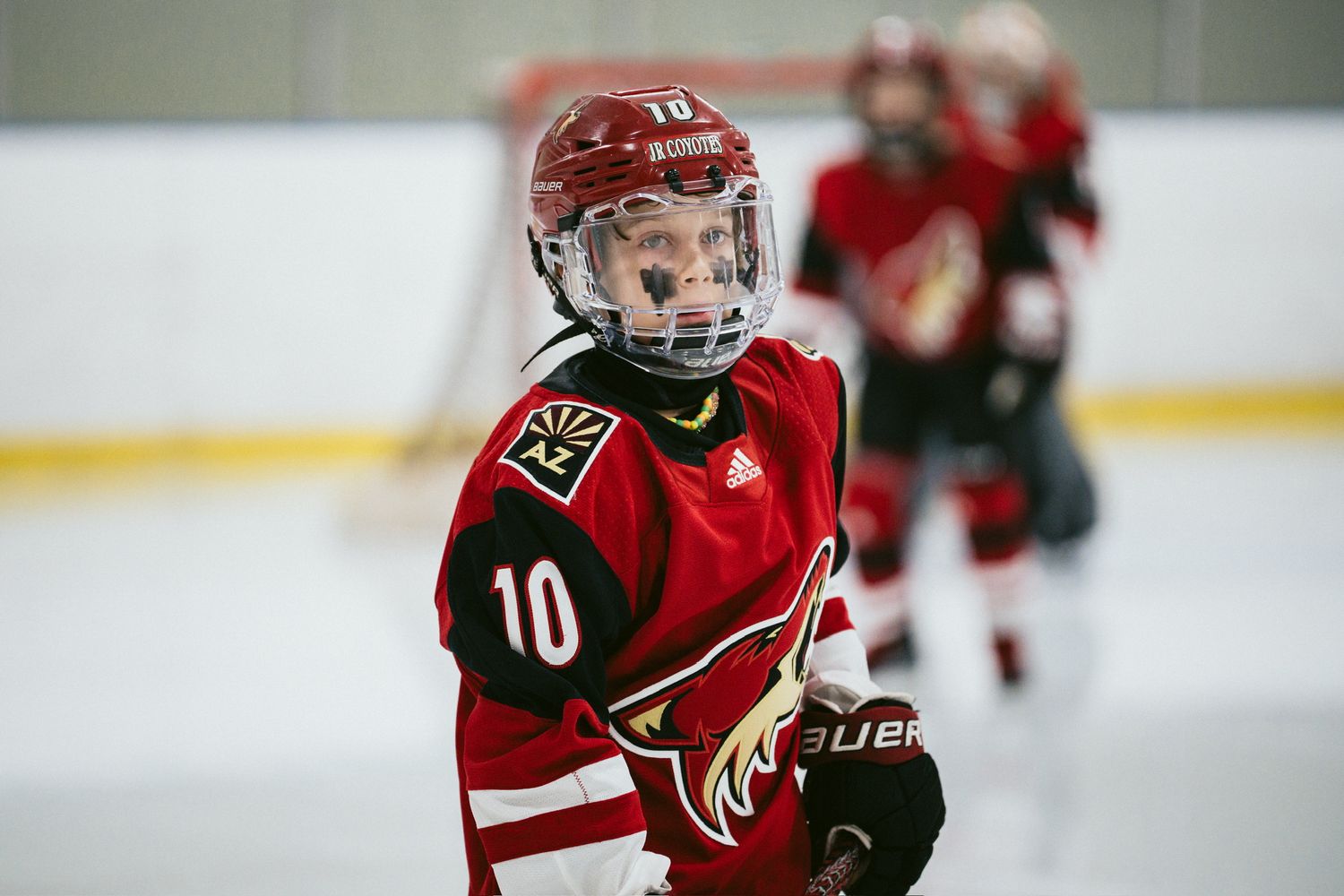 Youth hockey player in red Coyotes jersey number 10 skating during game.