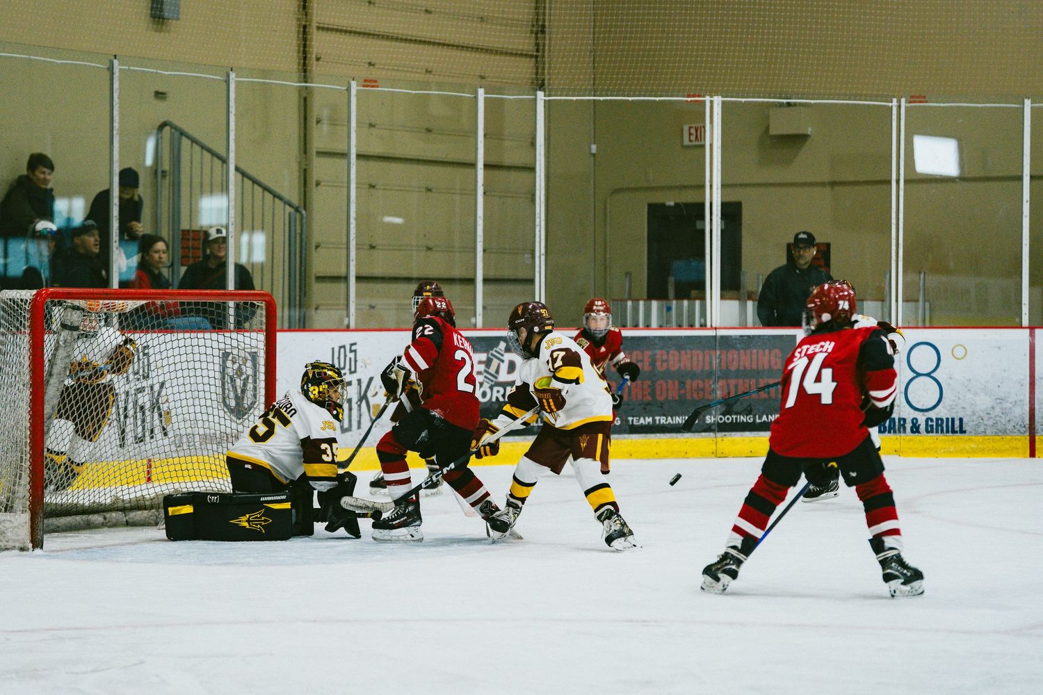 Intense hockey action near the goal with players from red and yellow teams battling for the puck.