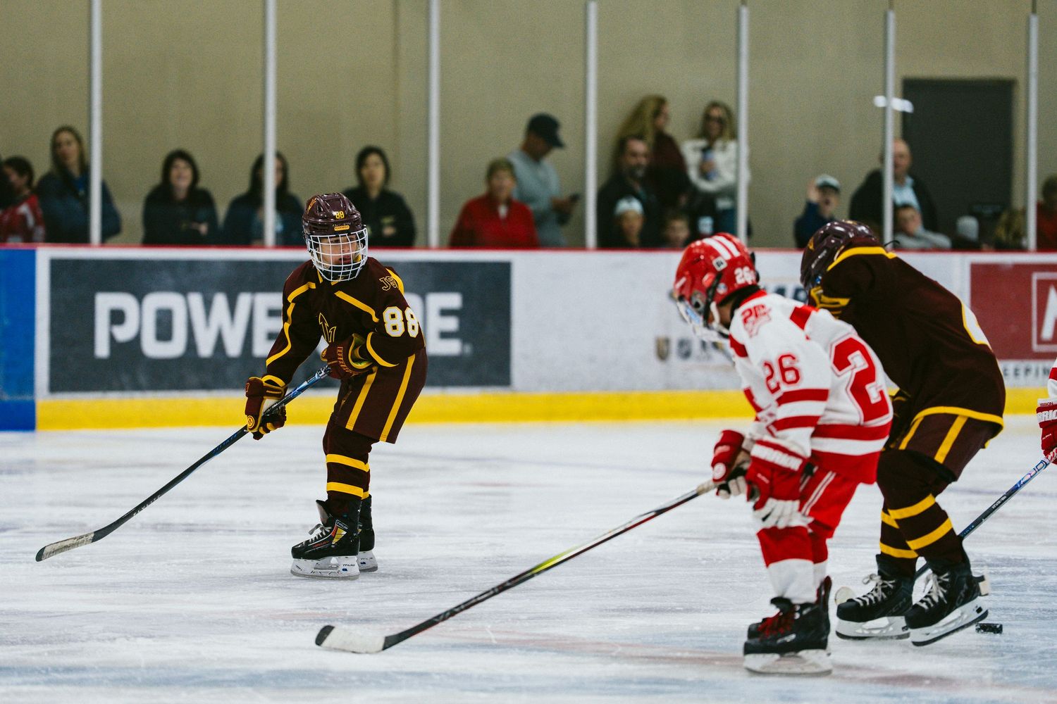Hockey players from opposing teams in red and black uniforms facing off on the ice.