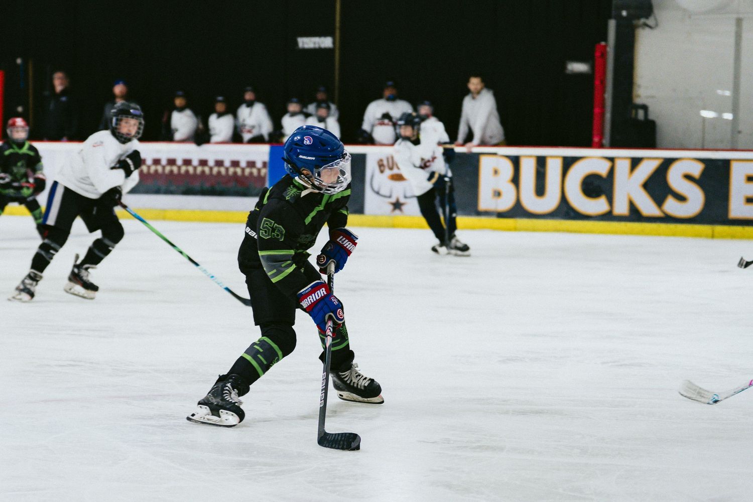 Young hockey players in black uniforms practicing skating and stickhandling on indoor ice rink.