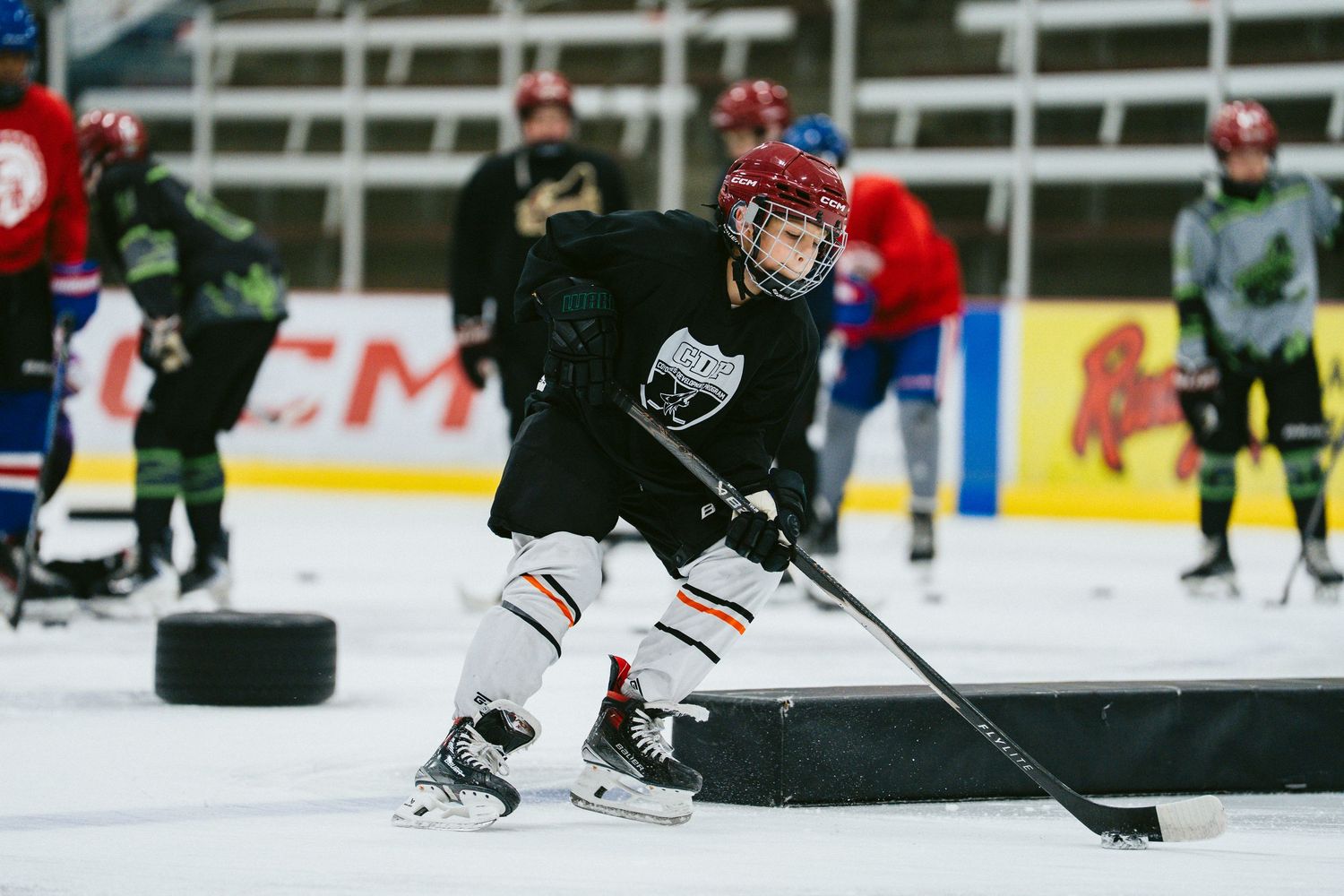 Youth hockey player in red helmet practicing puck handling skills during indoor ice hockey training.
