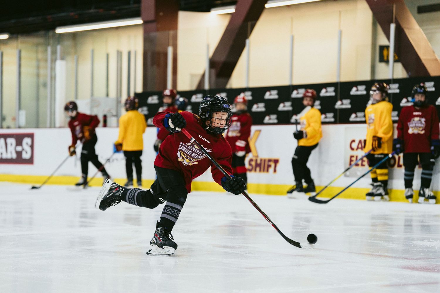 Young ice hockey player in red uniform taking a powerful shot on ice during team practice drill.