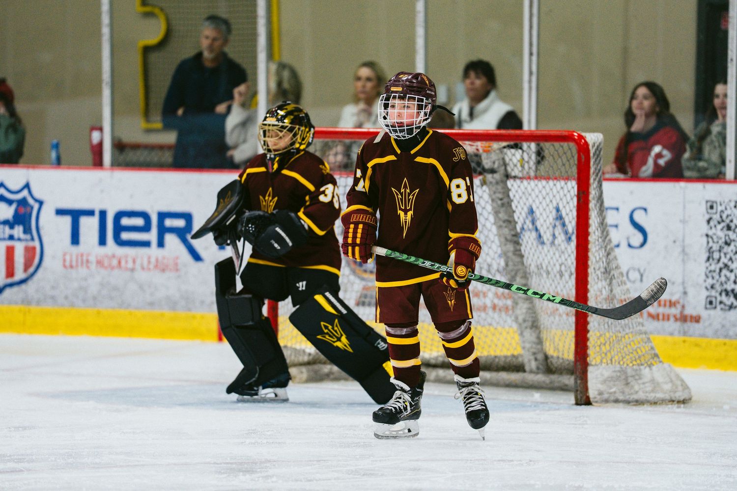 Hockey players in black and red uniforms competing near the goal during an ice hockey match.