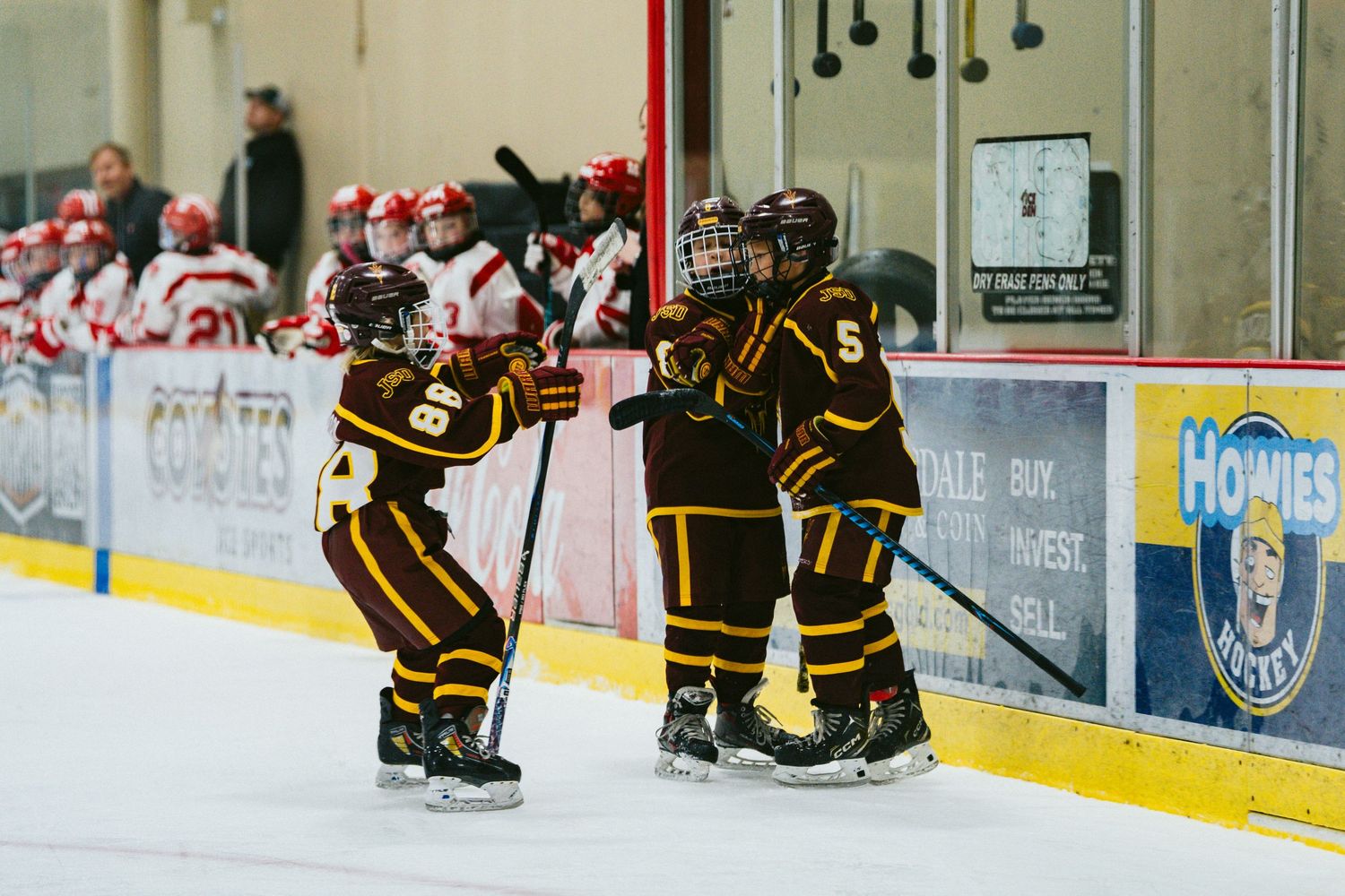 Wide view of an ice hockey rink showing players in action with spectators watching from the sidelines.