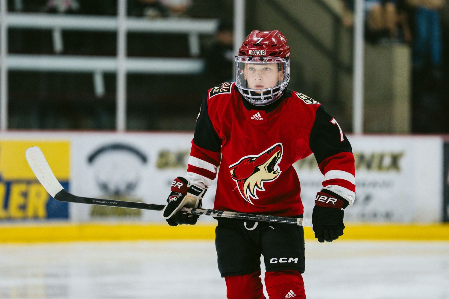 Young hockey player in red and black Phoenix Coyotes jersey skating on ice during youth hockey game.