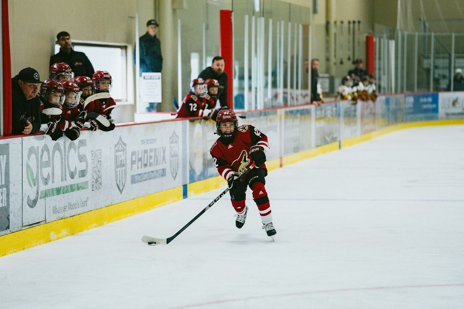 Hockey player in red jersey skates with the puck during competitive game on ice rink.