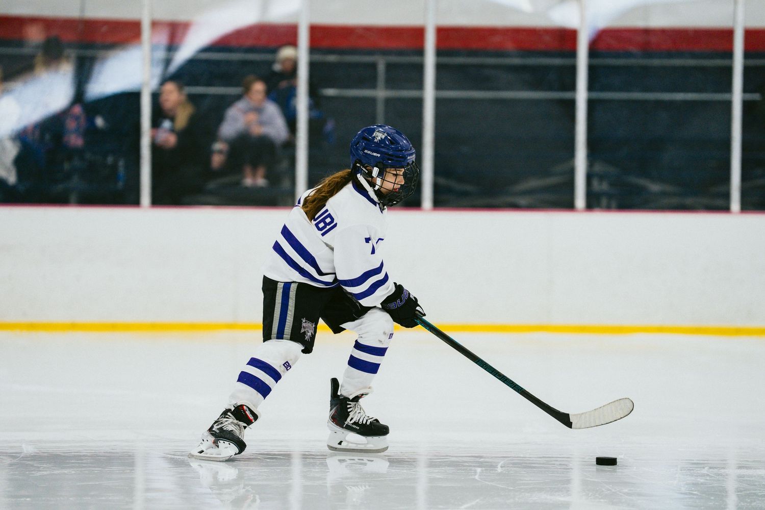 Hockey player in white striped jersey controls puck while skating.