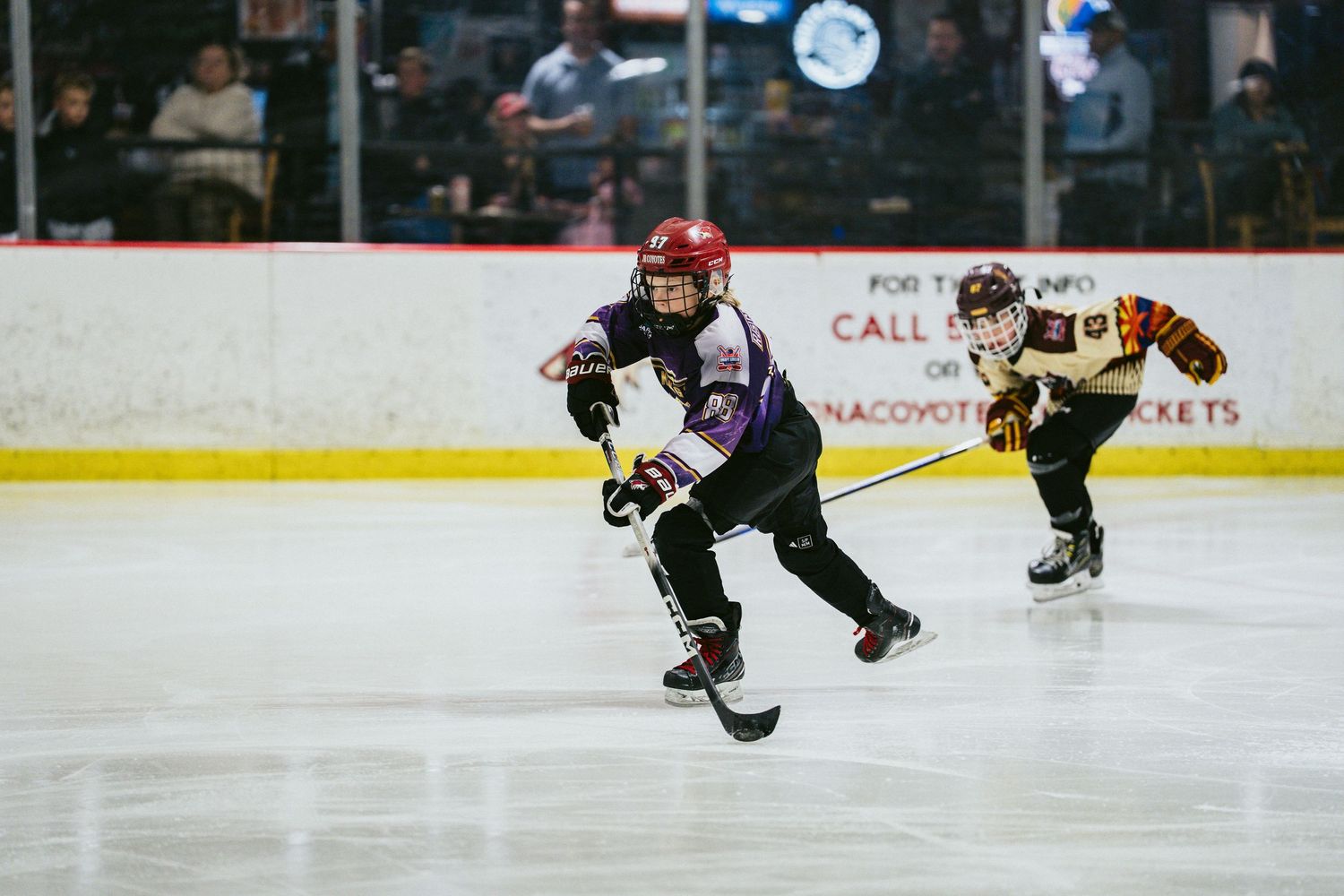 Two youth hockey players race for the puck during a competitive ice hockey game.