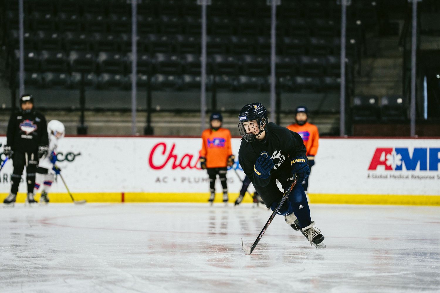 Youth hockey player skating with stick during ice hockey training session in indoor rink.