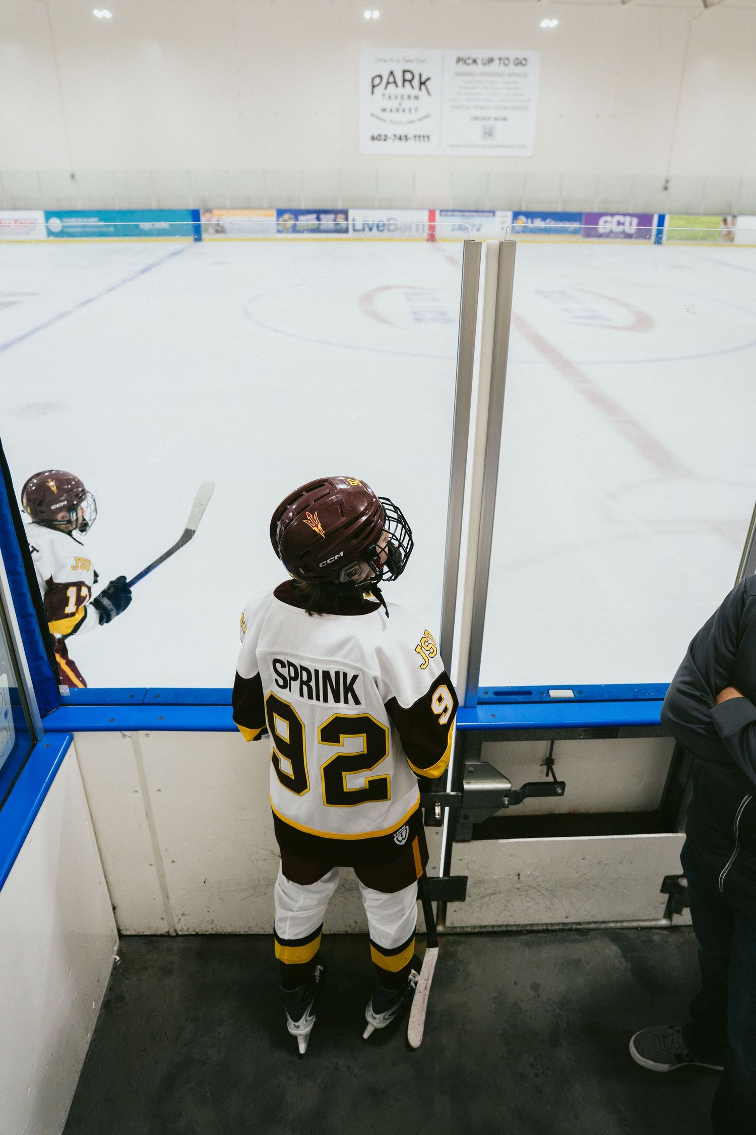 Young hockey player wearing jersey number 92 with name Sprink stands at the open gate to the ice.
