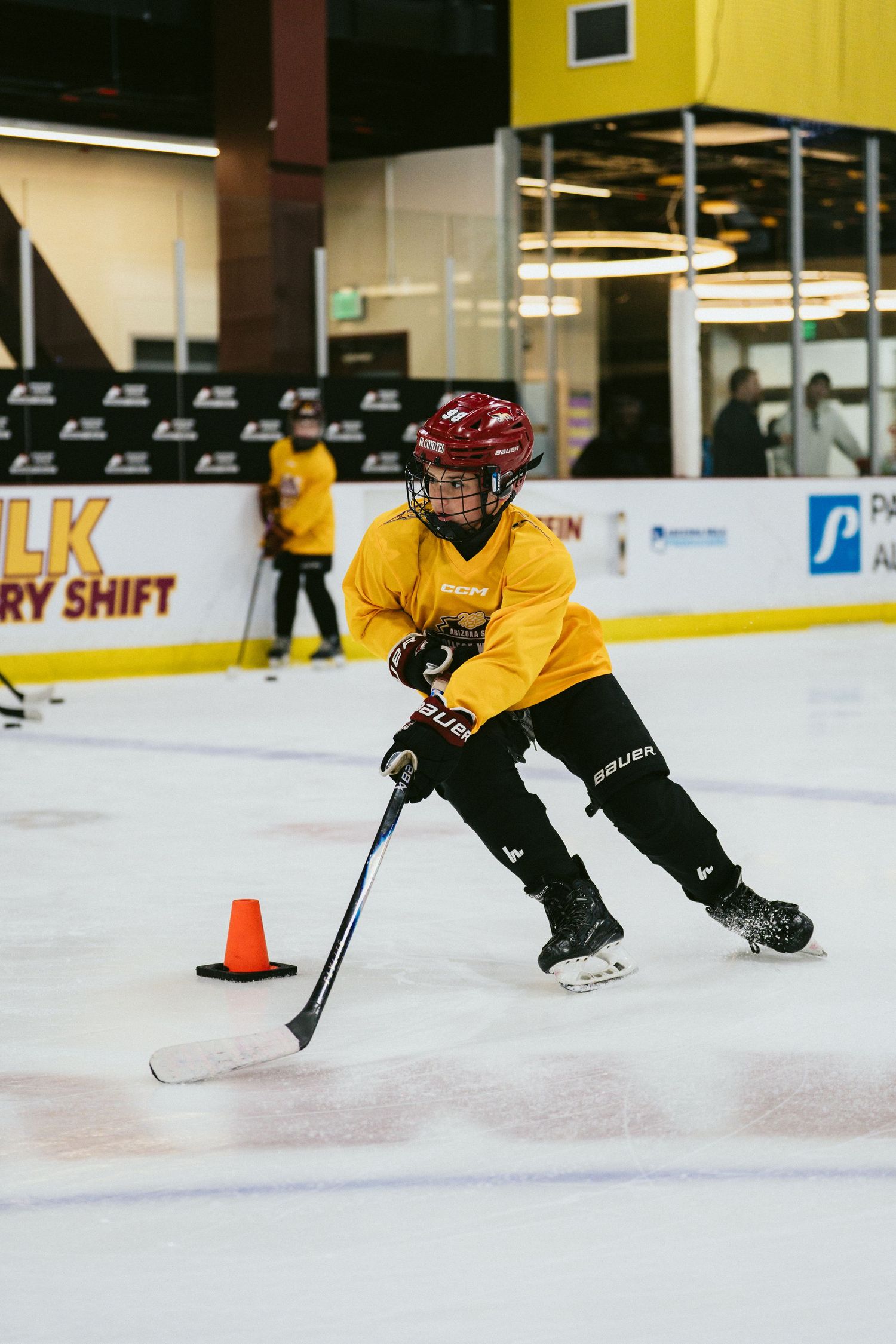 Young hockey player in yellow jersey executes a sharp turn around an orange cone during ice skating drills.