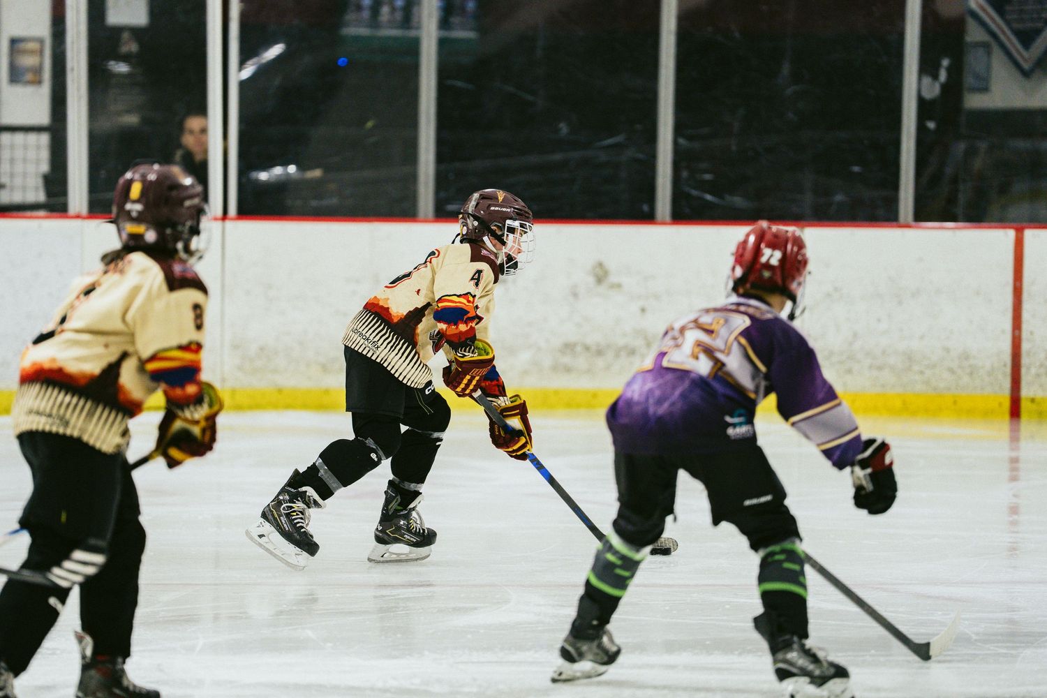 Youth hockey players compete on ice, with players in gold and purple uniforms facing off during a game.