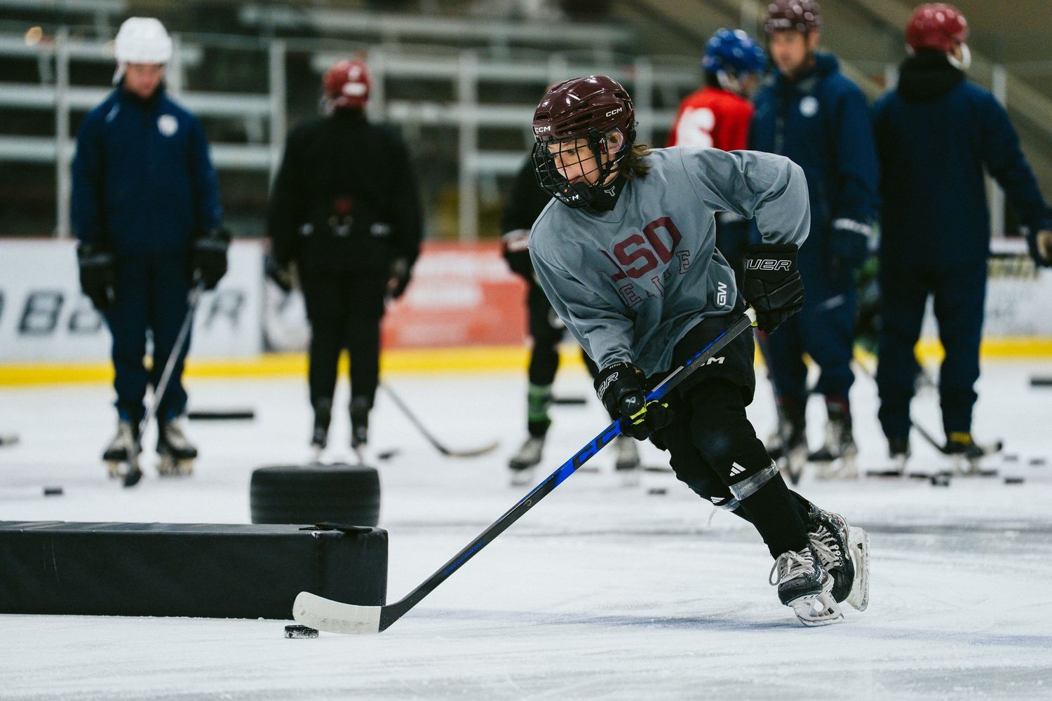 Youth hockey player in USA jersey practices puck control drills on ice during training camp session.