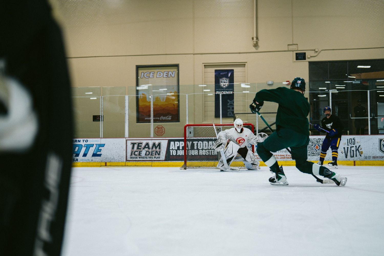 Hockey players compete on an indoor ice rink during a fast-paced game with team banners visible.