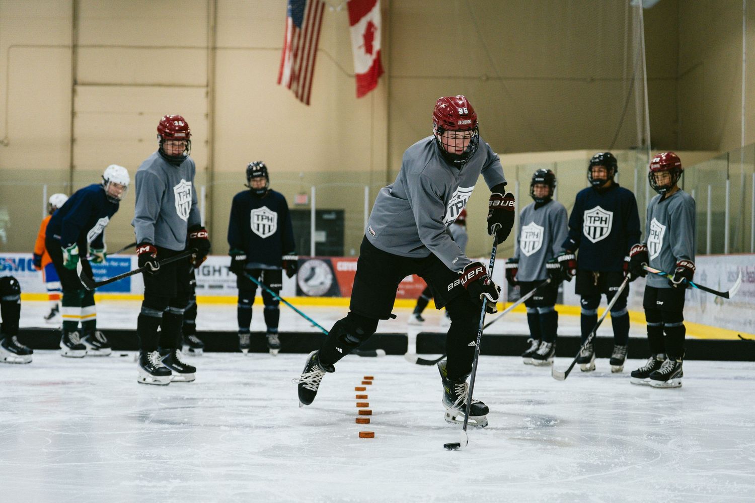 Hockey players practice skating drills on an indoor ice rink during a team training session with coaches observing.