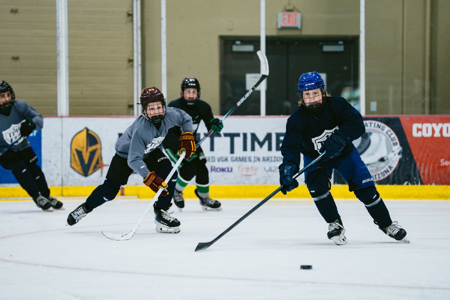 Two youth hockey players compete for puck during ice hockey practice drill at indoor rink.