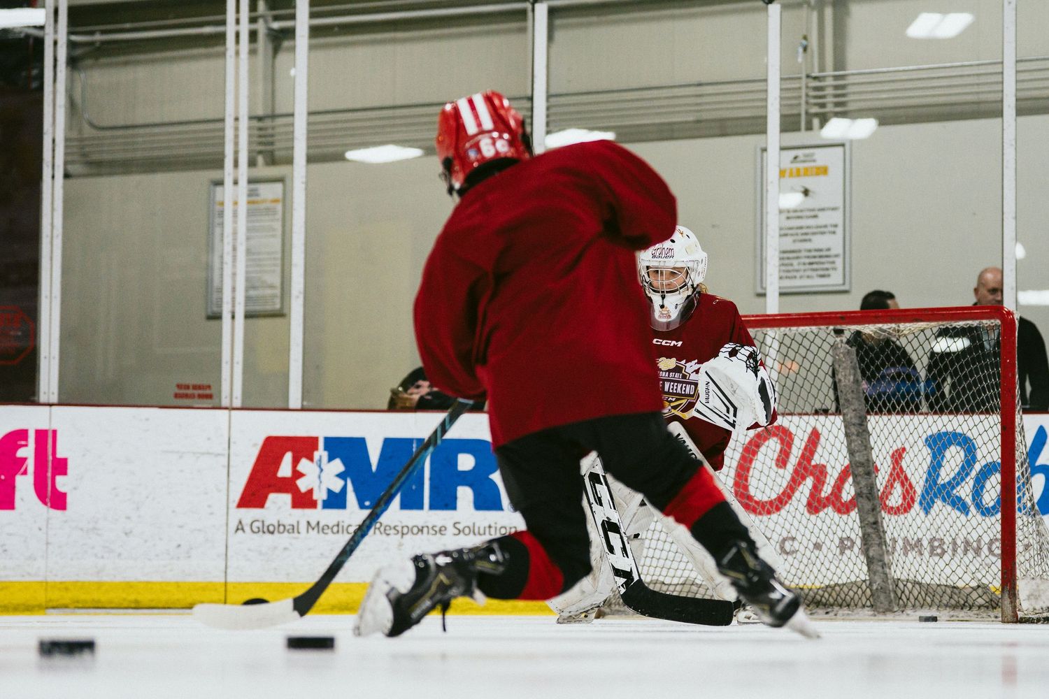 Young hockey player in red jersey skates toward the net during a youth ice hockey practice drill.
