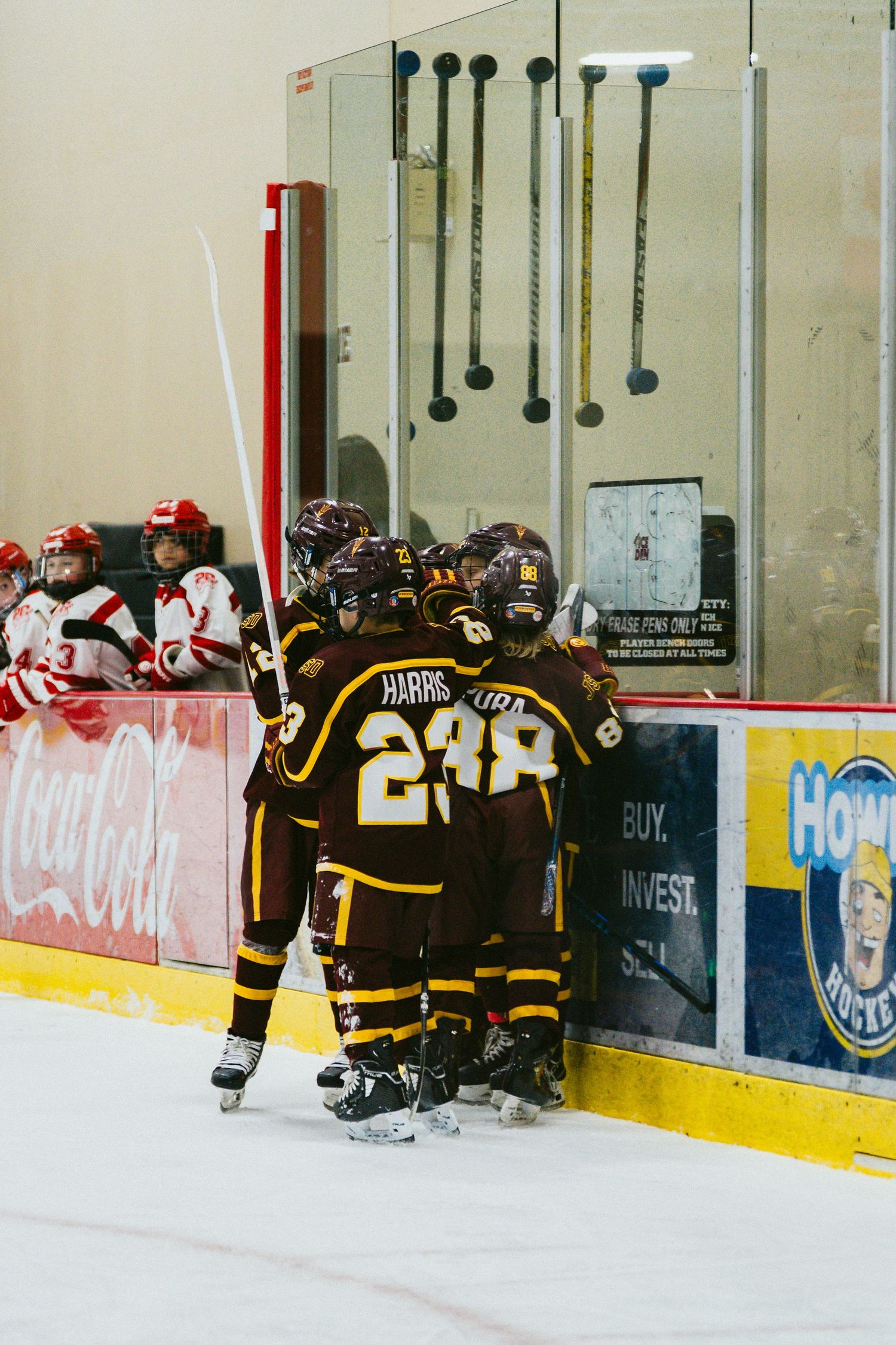 Hockey players in brown jerseys gather along the boards during a game break.