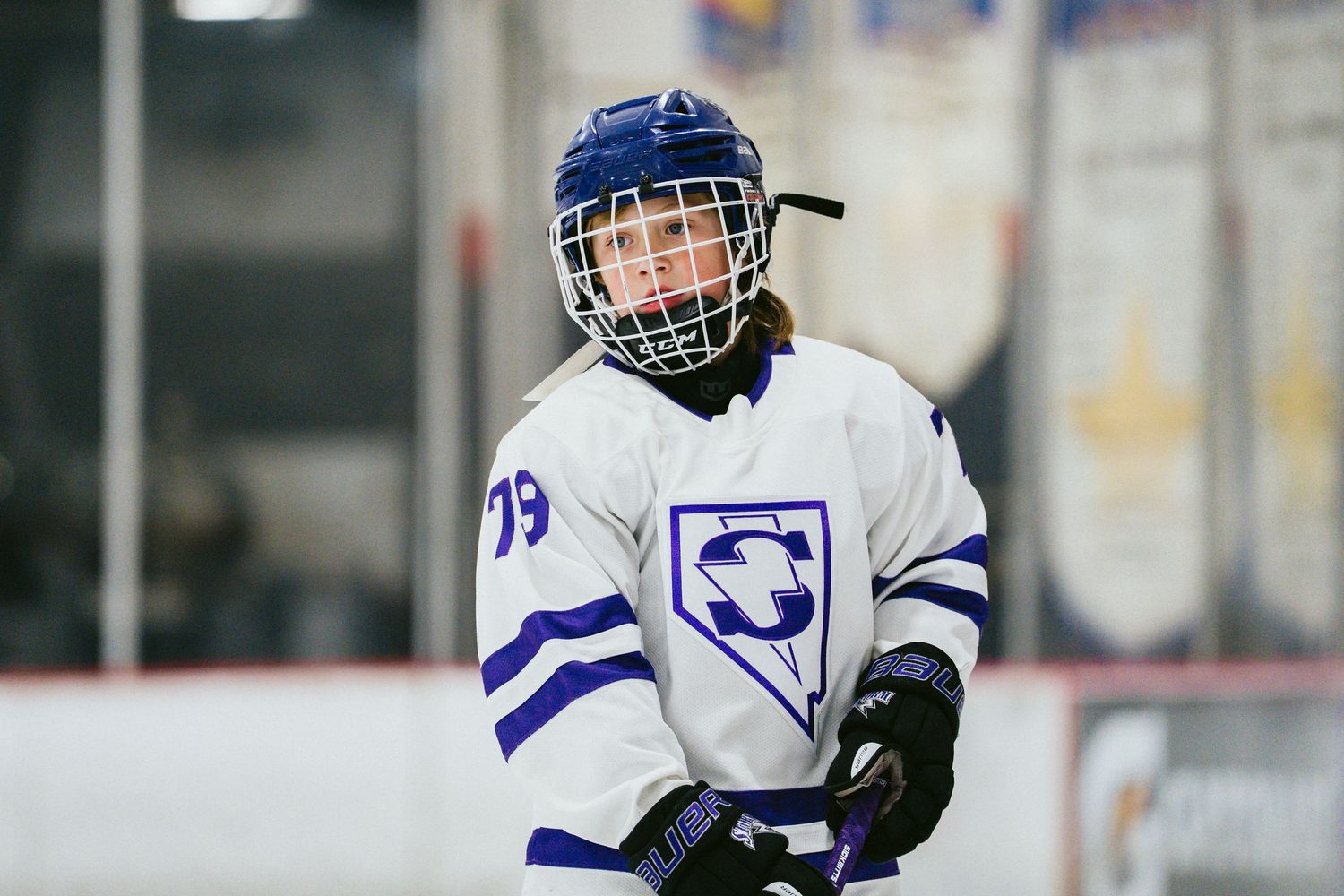 Youth hockey player in white and blue uniform skating on ice rink.