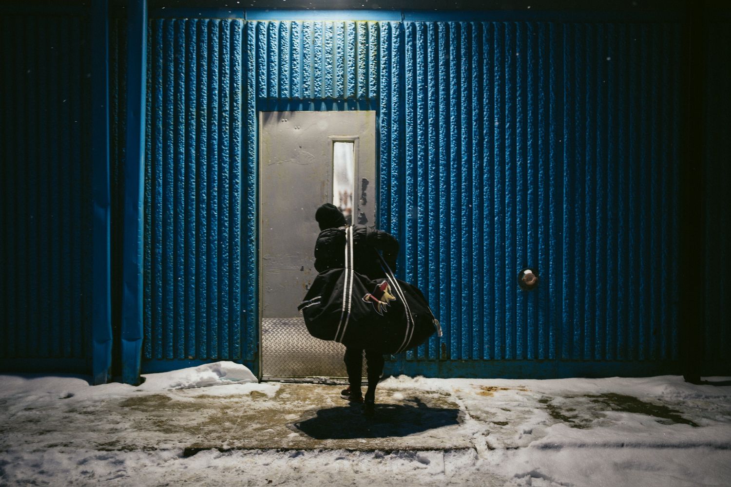 Snow covered exterior of a blue metal building at night.