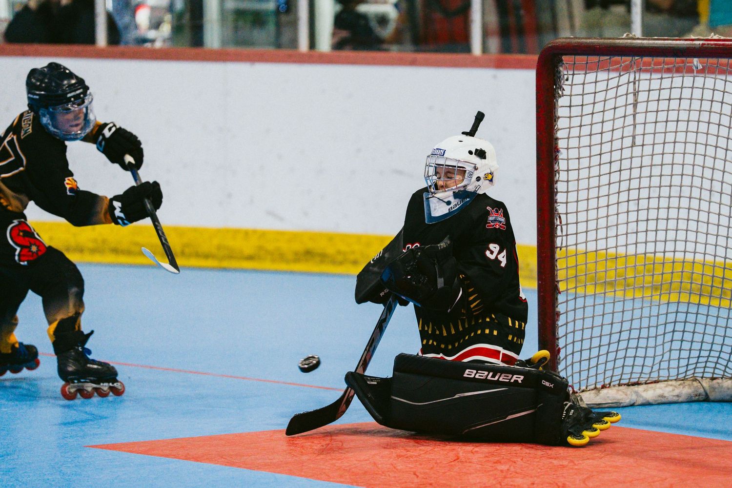 Roller hockey goalie makes a save attempt as opponent shoots on net during game.