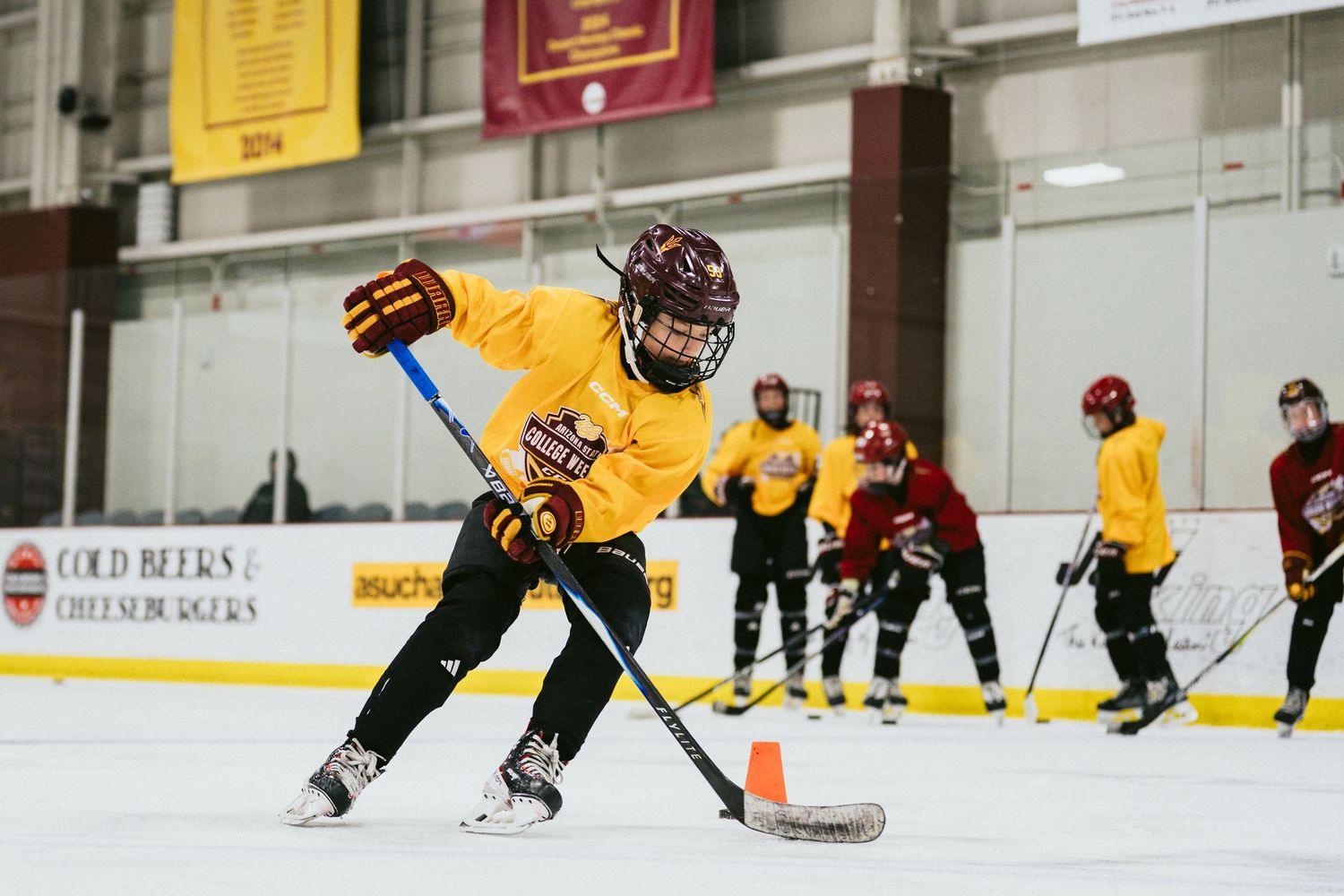 Young hockey player in yellow jersey practices stickhandling drills on an indoor ice rink.