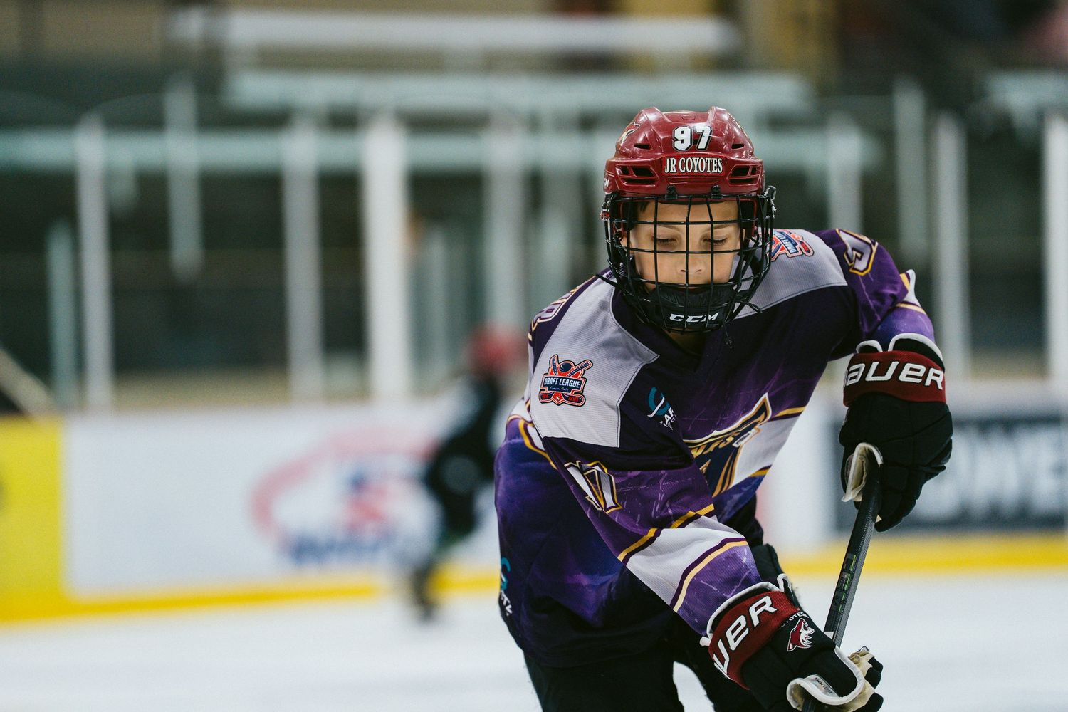 Youth hockey player wearing number 97 purple jersey and red helmet skating during competitive ice hockey game.