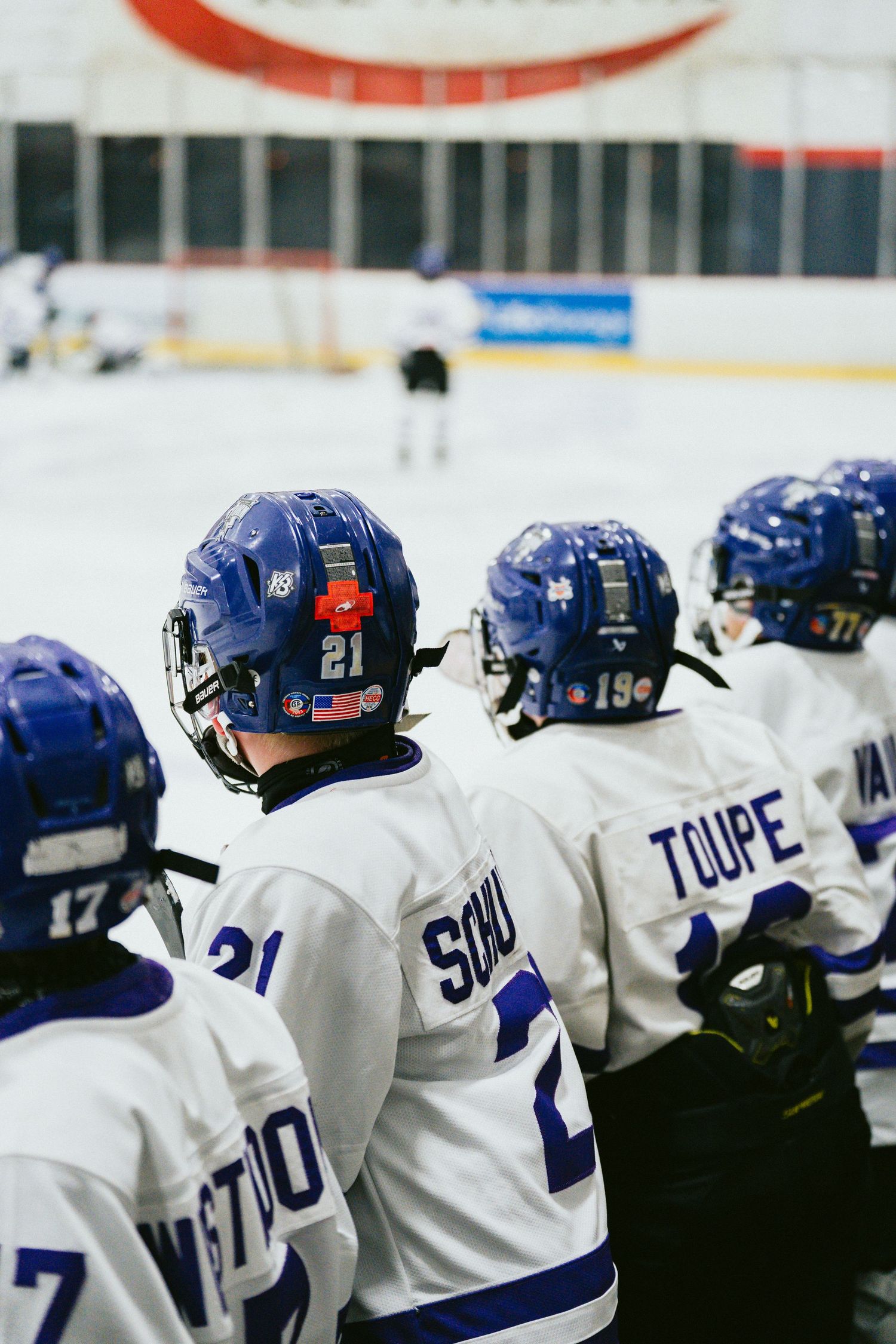 Row of hockey players on bench wearing blue helmets and white jerseys during game.