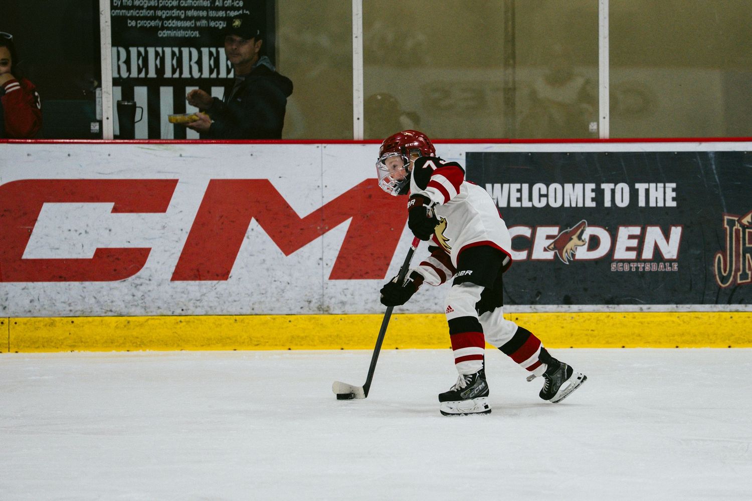 Players chase after the puck during an ice hockey match with arena advertisements visible.