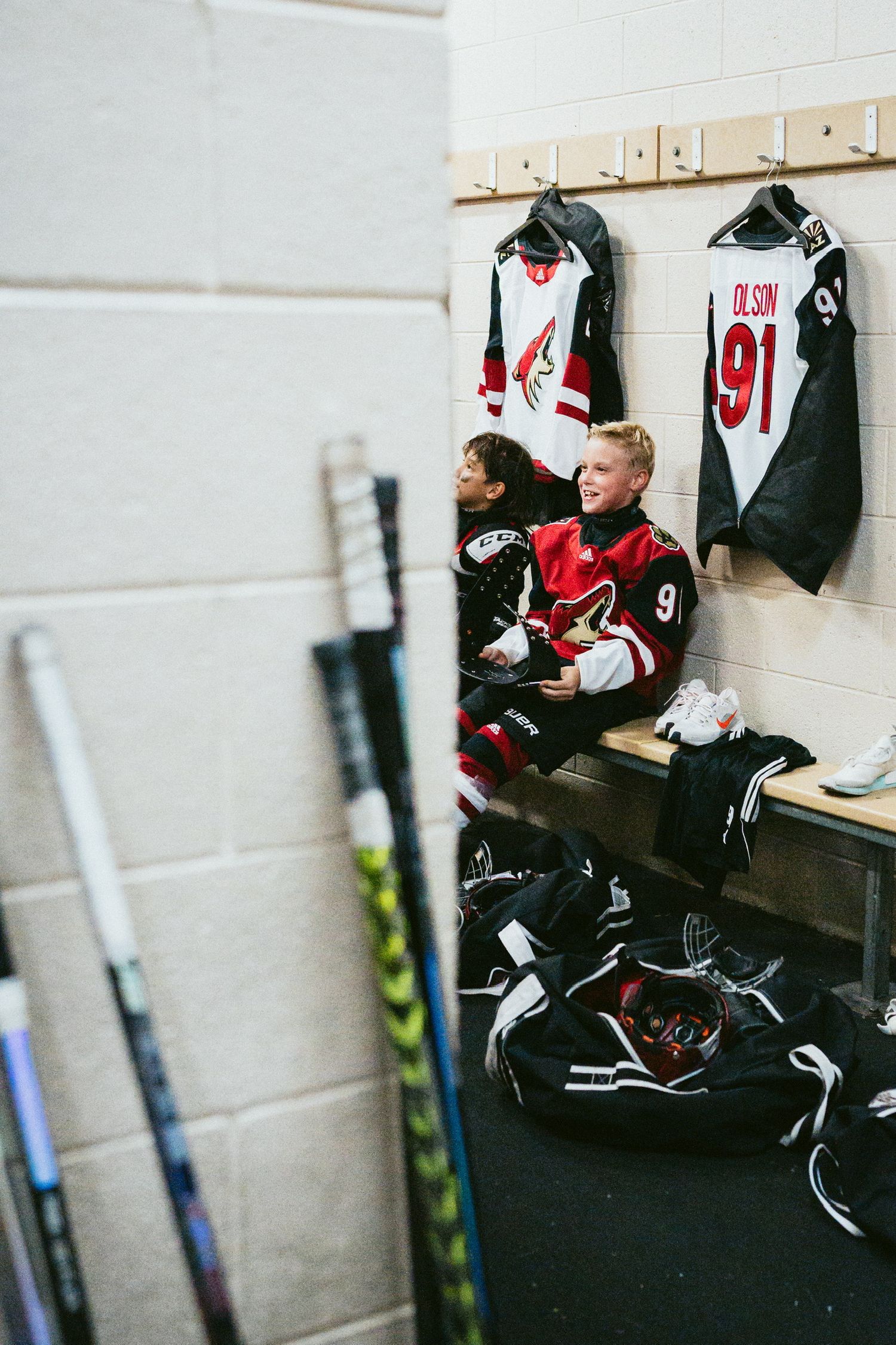 Hockey equipment and gear bags lined up in a locker room against white walls.