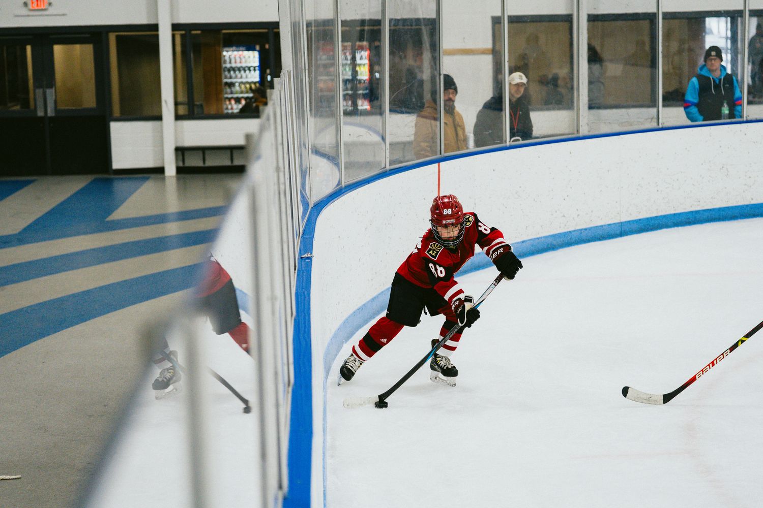 Hockey player in red uniform skates with stick on ice rink.