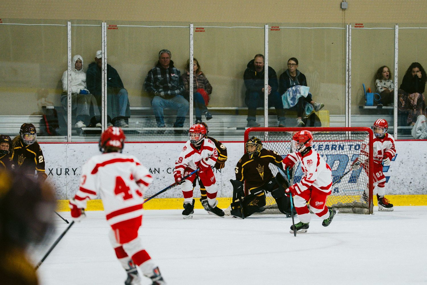 Ice hockey match between teams in red and black uniforms with spectators watching from the sidelines.