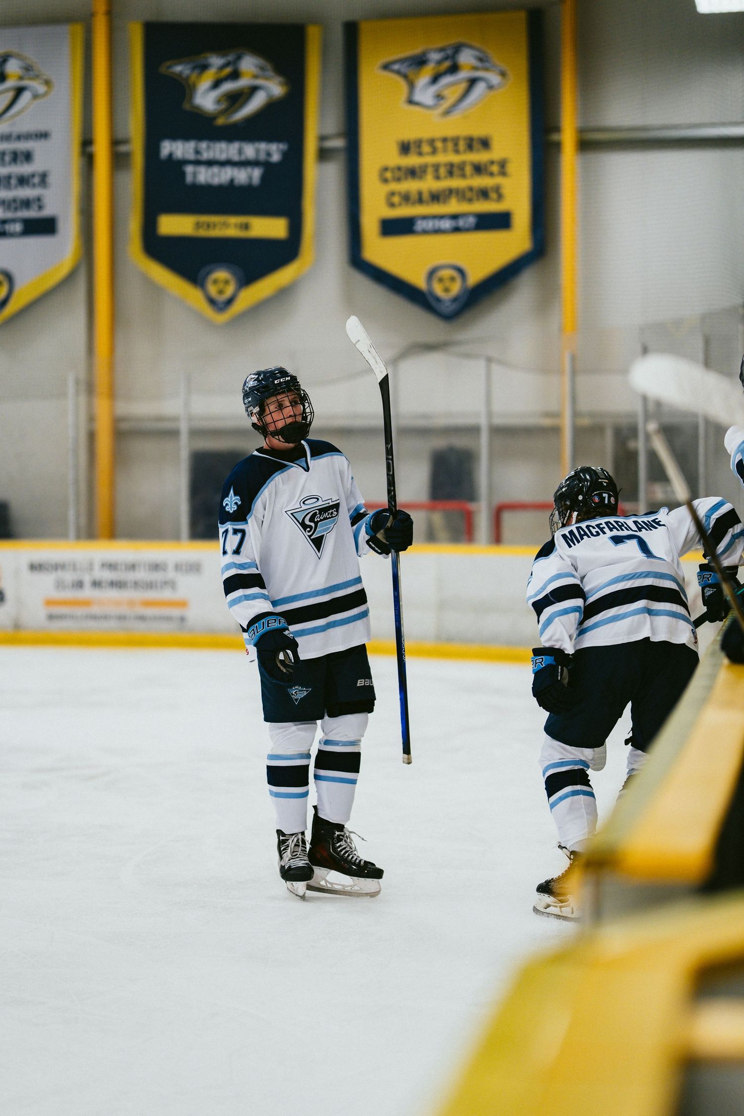 Youth hockey player #17 on ice rink with Nashville Predators banners, holding stick up in celebration.